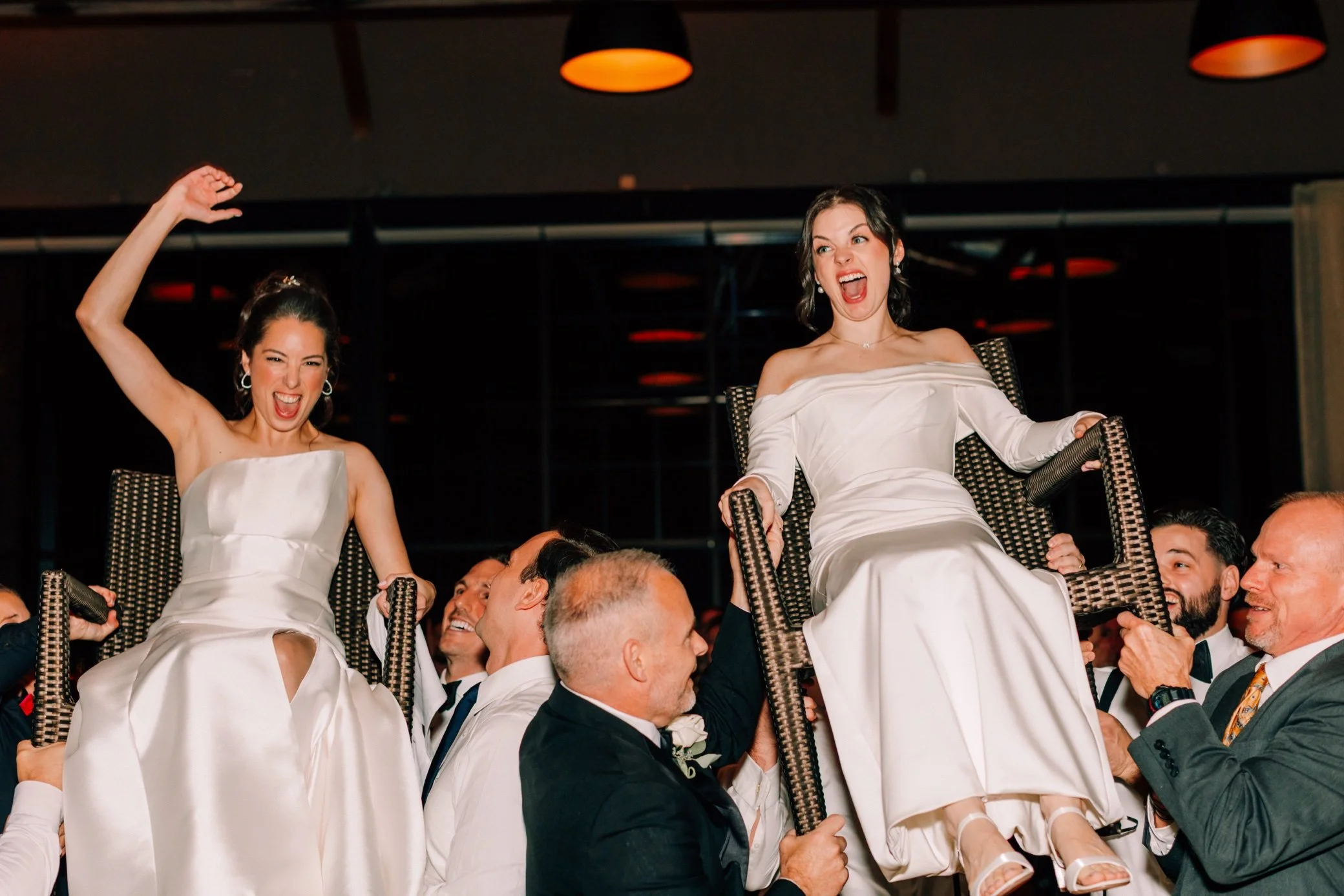  brides laughing and cheering while being lifted on chairs at the roundhouse 