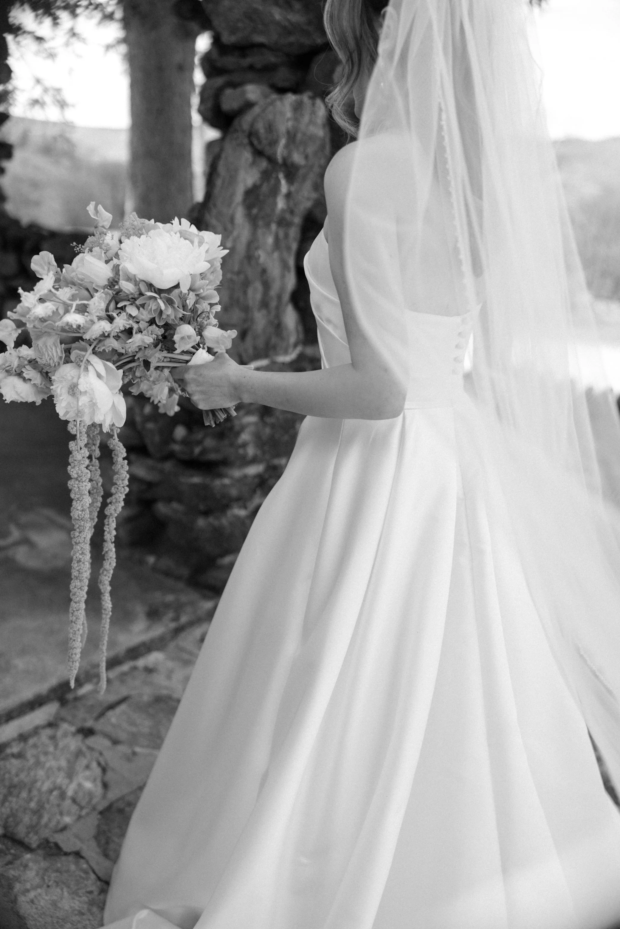 candid photograph of the back of bride's dress and veil holding her bouquet in her left hand walking into a stone gazebo in garrison new york