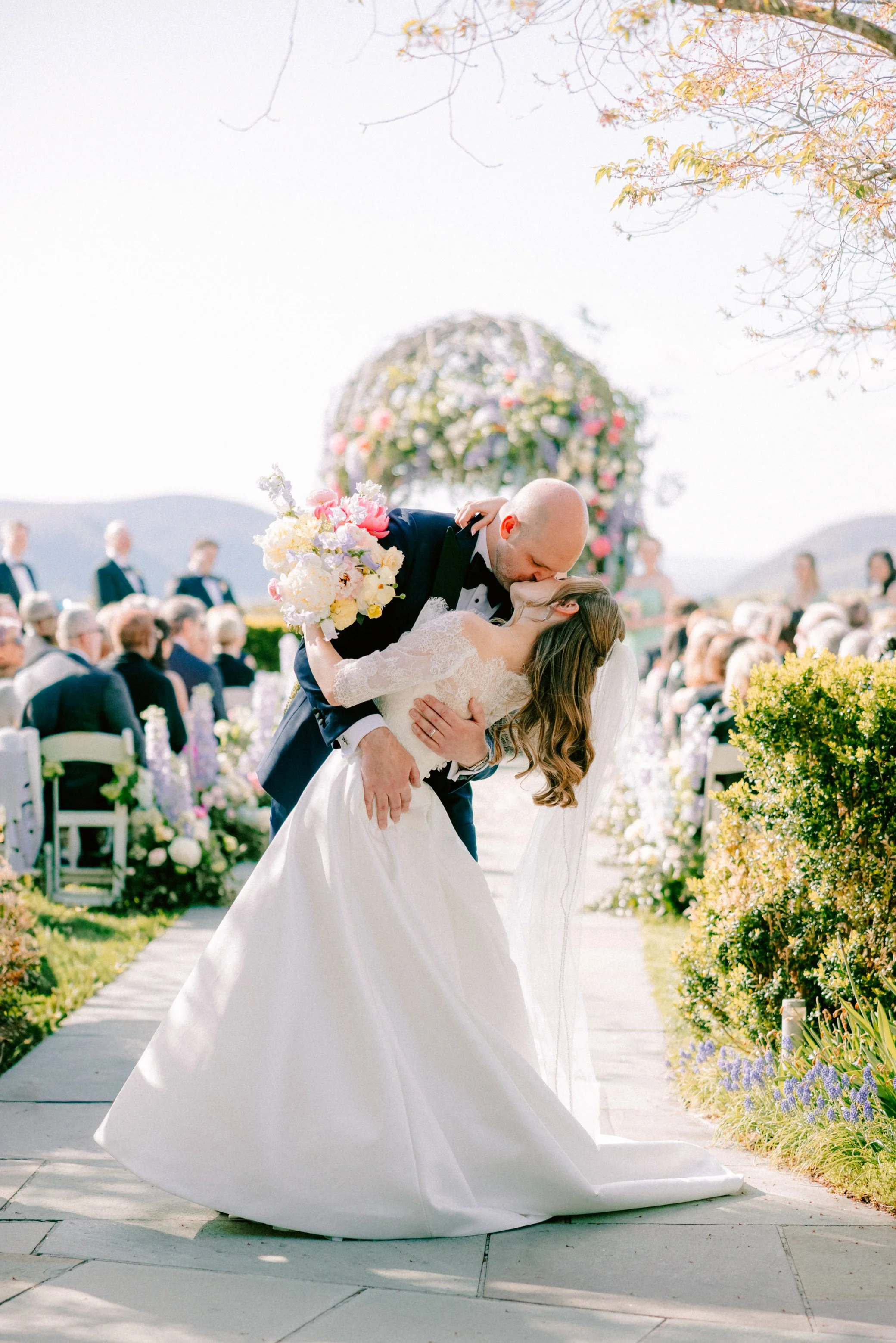 groom kissing bride and dipping her while she holds her bouquet in her left hand at the end of the wedding ceremony aisle in garrison new york