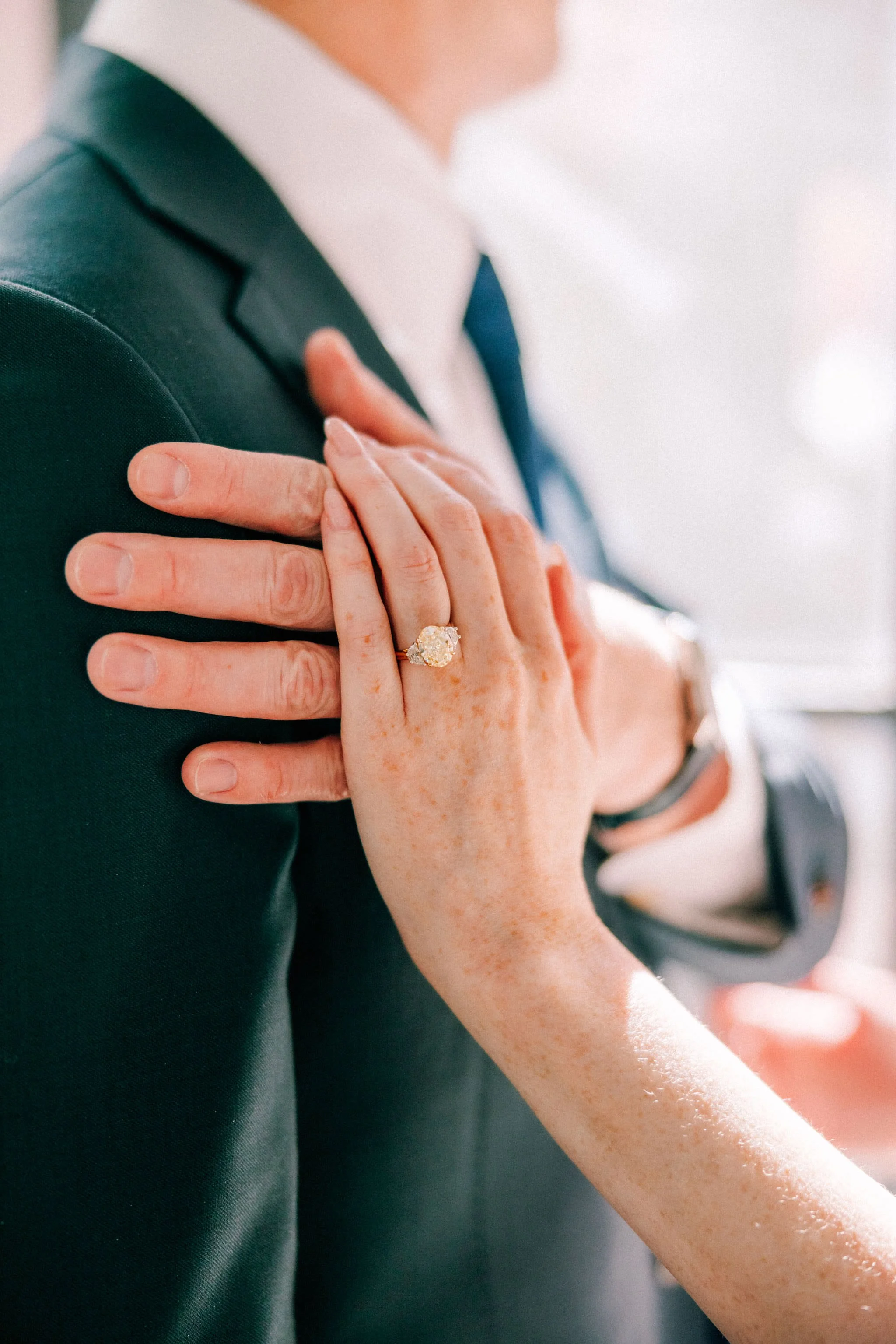 woman rests her hand on man wearing a suit's hand wearing a yellow diamond engagement ring during engagement photography shoot in brunette wine bar