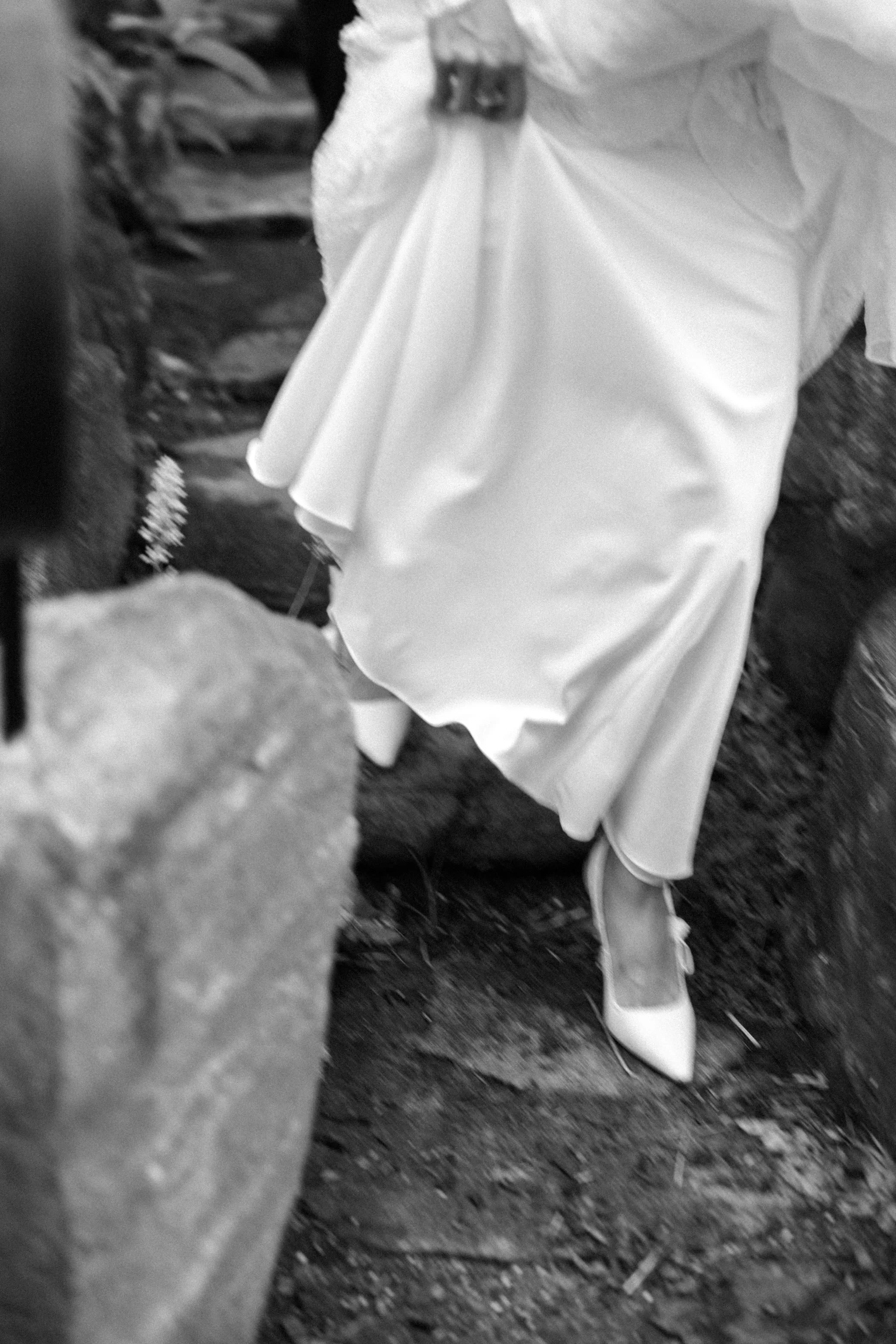 black and white photograph of bride holding up her dress walking down stone steps on her wedding day at untermyer gardens