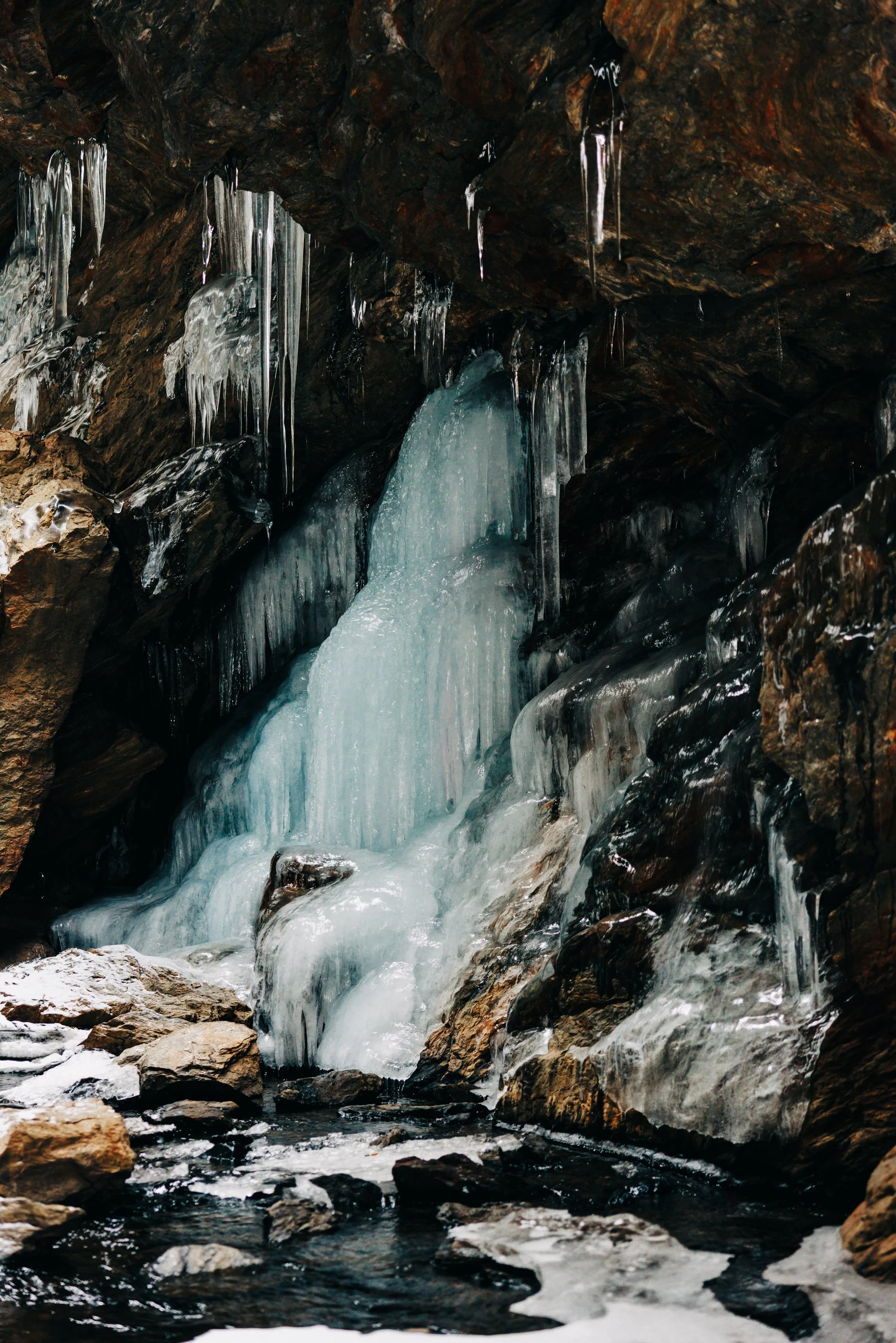 Photograph of a partially frozen waterfall with ice and icicles on rocky terrain at Dover Stone Church by Caitlinn Mahar-Daniels, hudson valley wedding photographer.