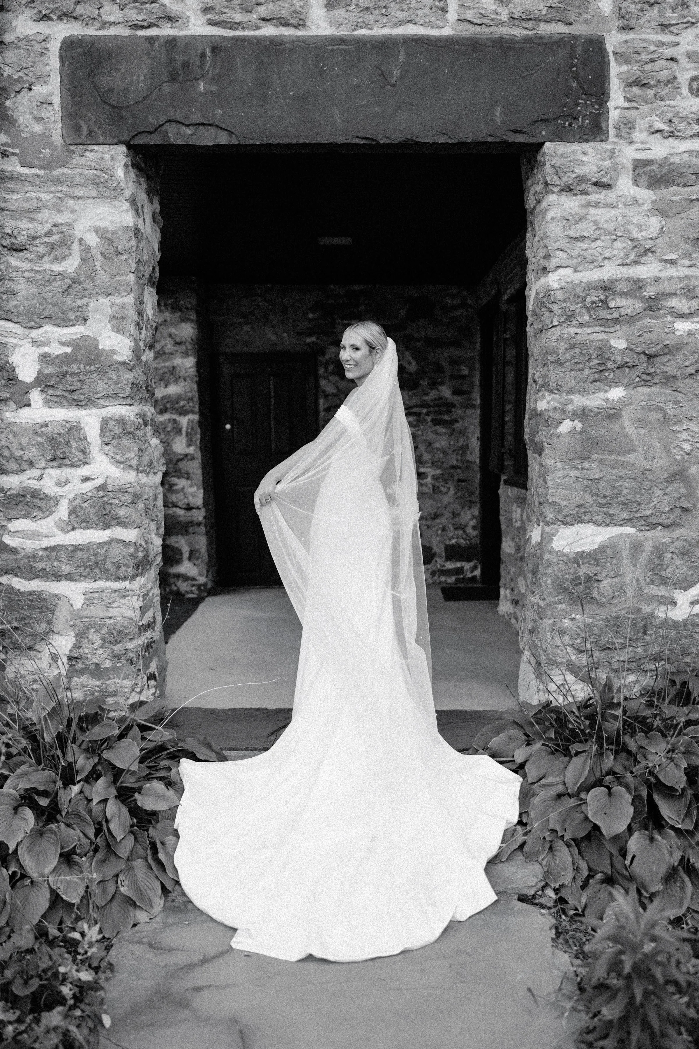 black and white photograph of bride holding her veil and turning around on her wedding day at the senate garage