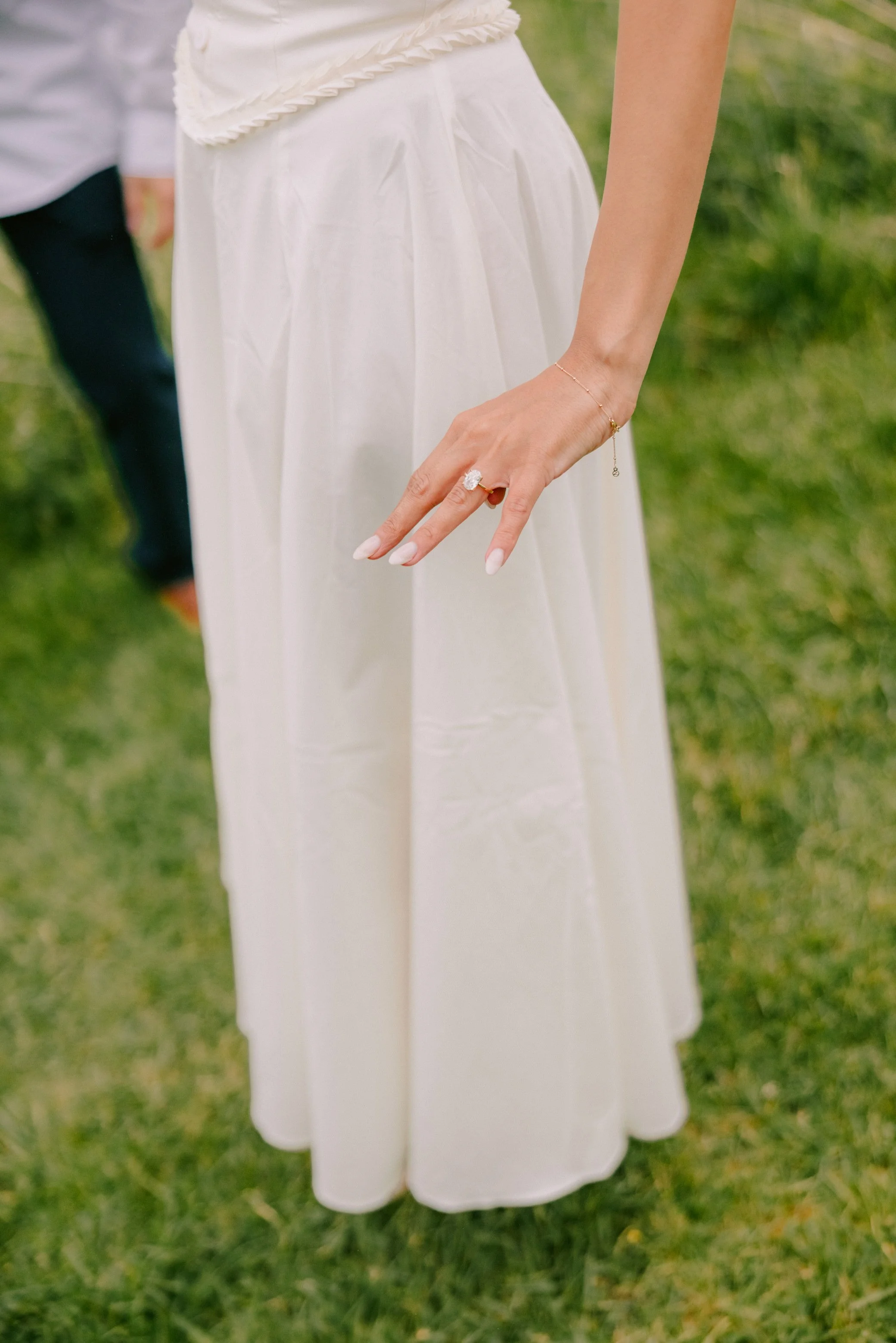 woman wearing white dress holds out hand with engagement ring after she was just proposed to at kenoza hall