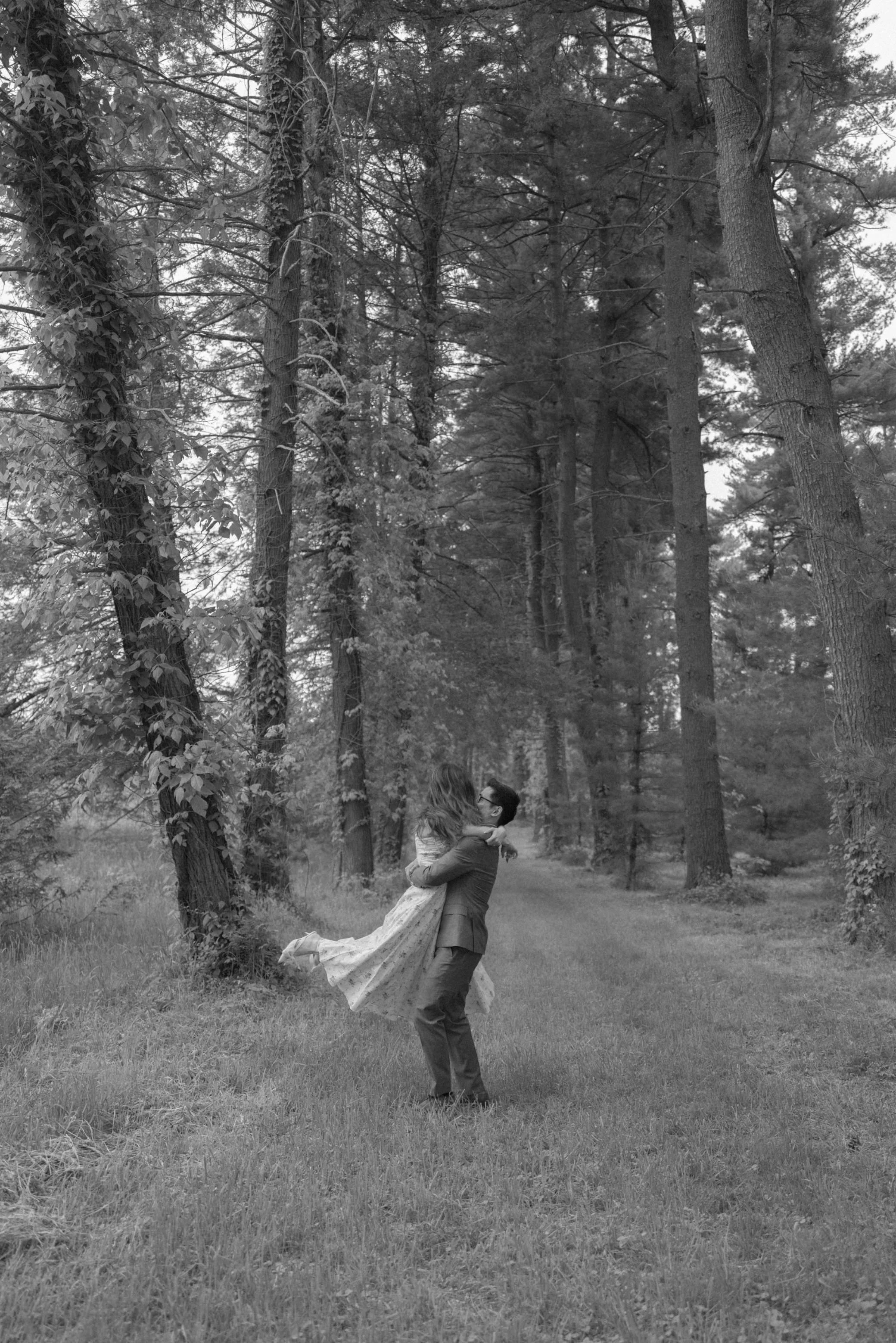 engaged couple embrace and spin in the woods during their engagement photo shoot at vanderbilt mansion