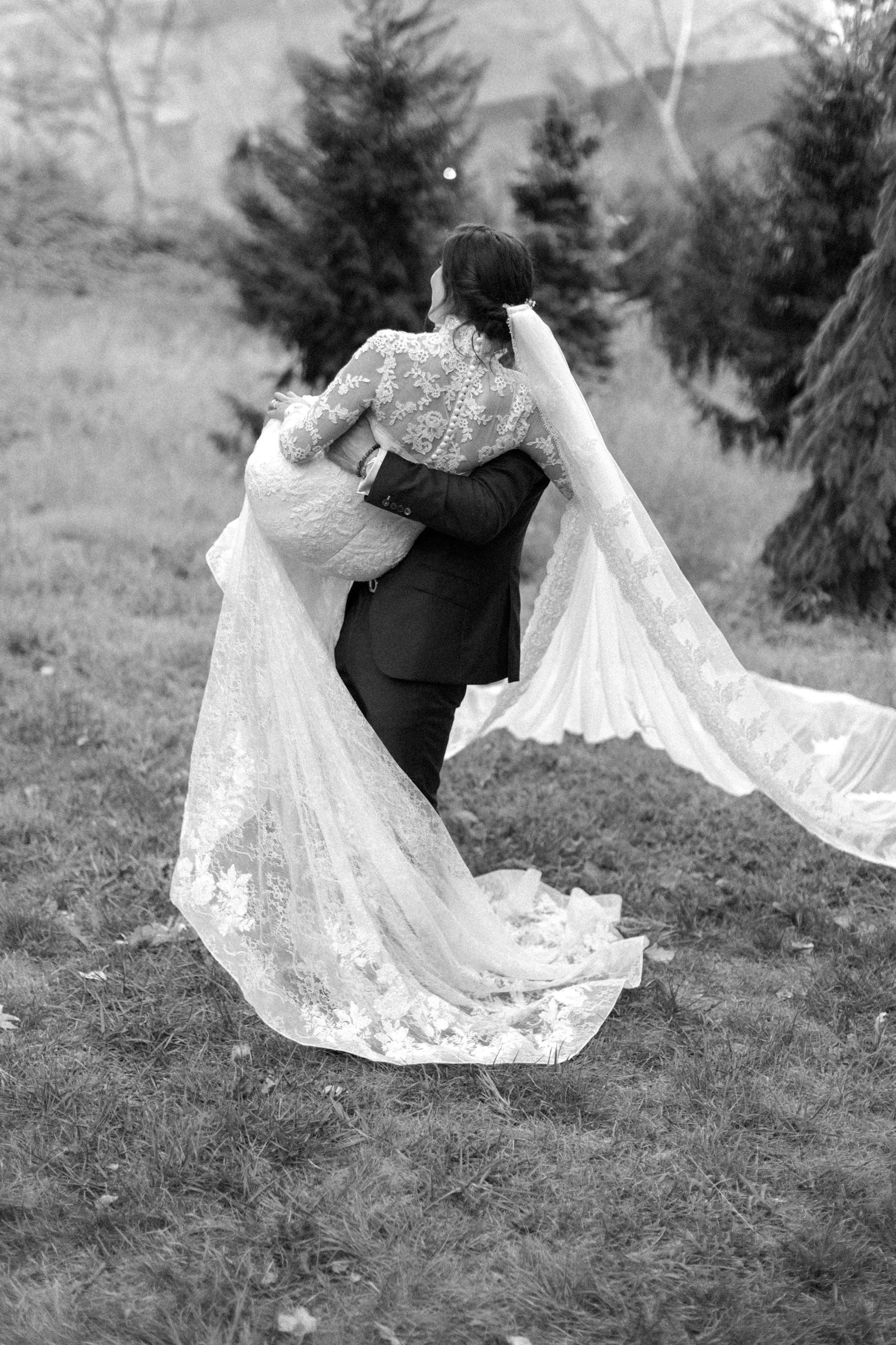 black and white photograph of groom picking p his bride wearing long sleeve lace dress and cathedral length veil at the Temple of Love in Untermyer Gardens on their wedding day