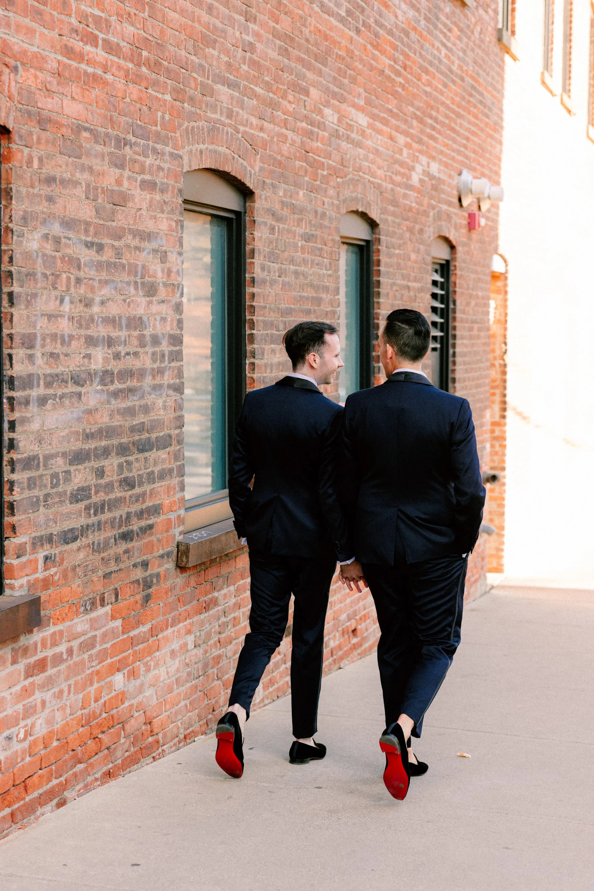 grooms look at each other while walking away showing off their red bottom christian louboutin shoes on their wedding day at the roundhouse in beacon ny
