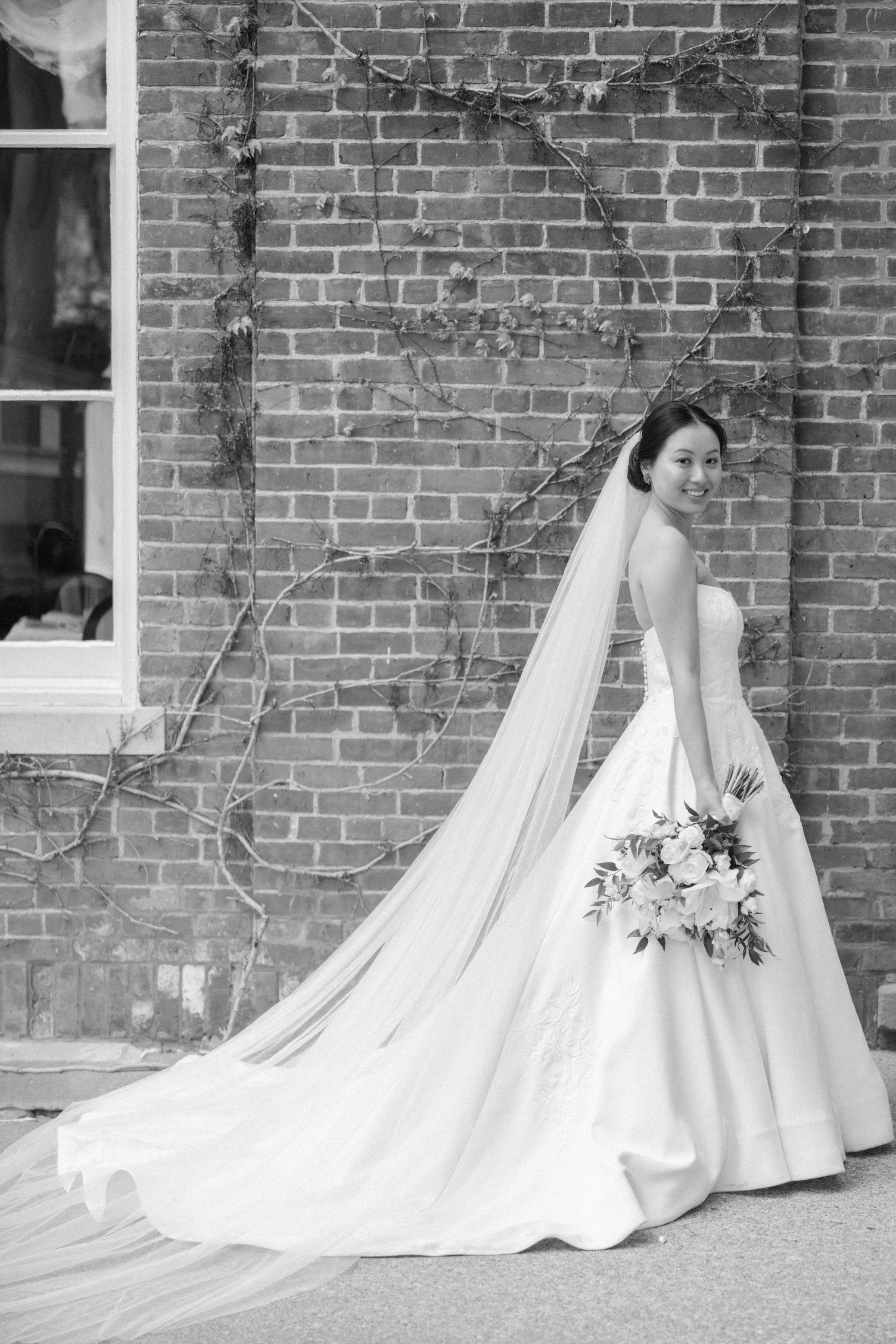 timeless photograph of bride looking over her right shoulder with her bouquet at her side in front of brick exterior of otesaga hotel