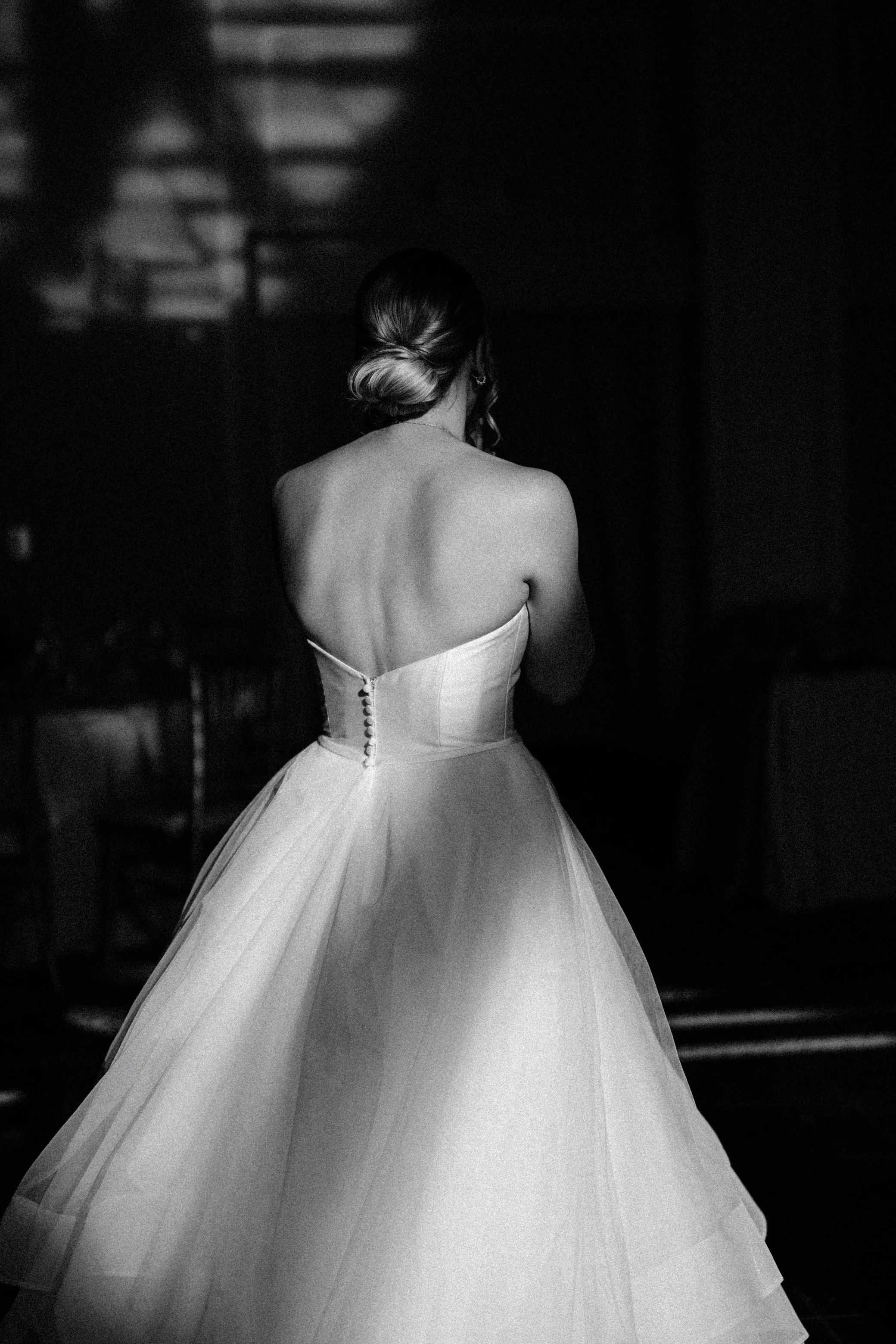 black and white photograph with dramatic lighting of a bride's back walking into her reception space on her wedding day at le chateau