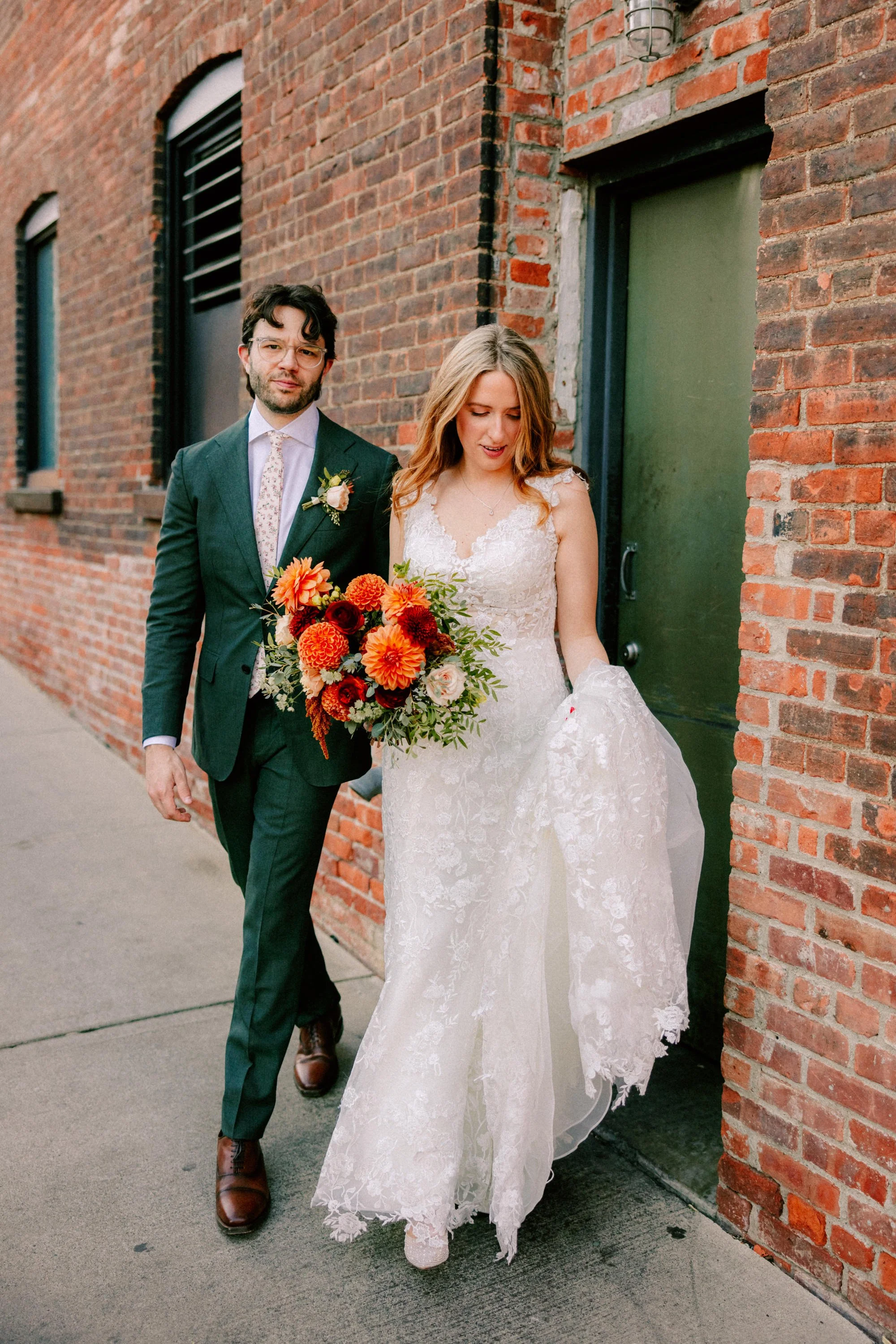 wedding couple walk in front of brick wall at the roundhouse