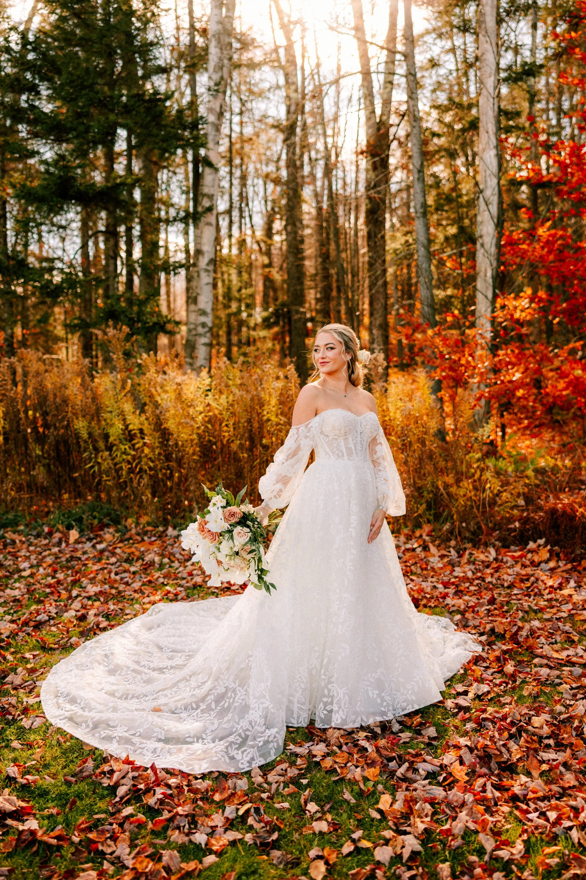 bride standing in fallen leaves looking over her shoulder in the fall foliage on her wedding day at Mountaintop Resort in Vermont
