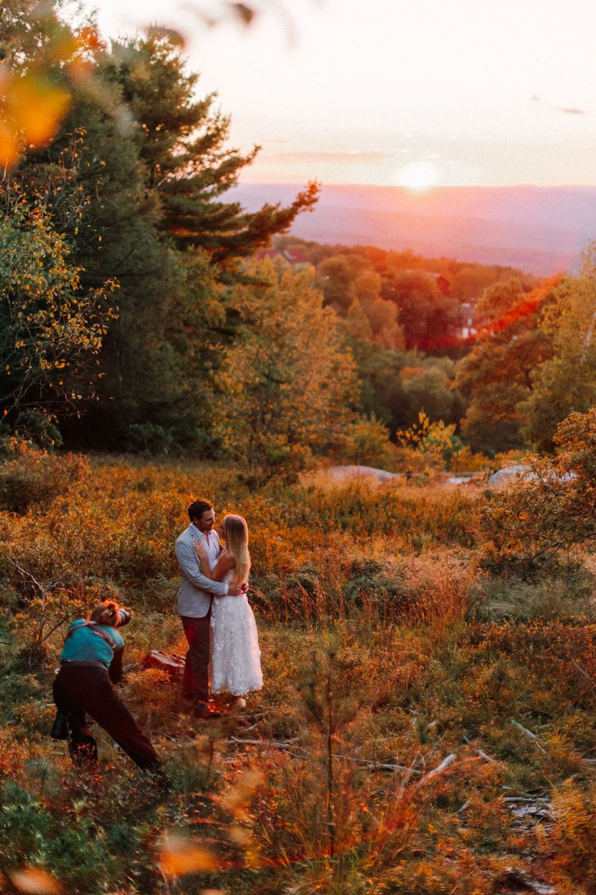 A couple in wedding attire stands close together in an autumn landscape during sunset, with Caitlinn Mahar-Daniels, hudson valley wedding photographer, capturing the moment during a surprise proposal at Mohonk Mountain House.