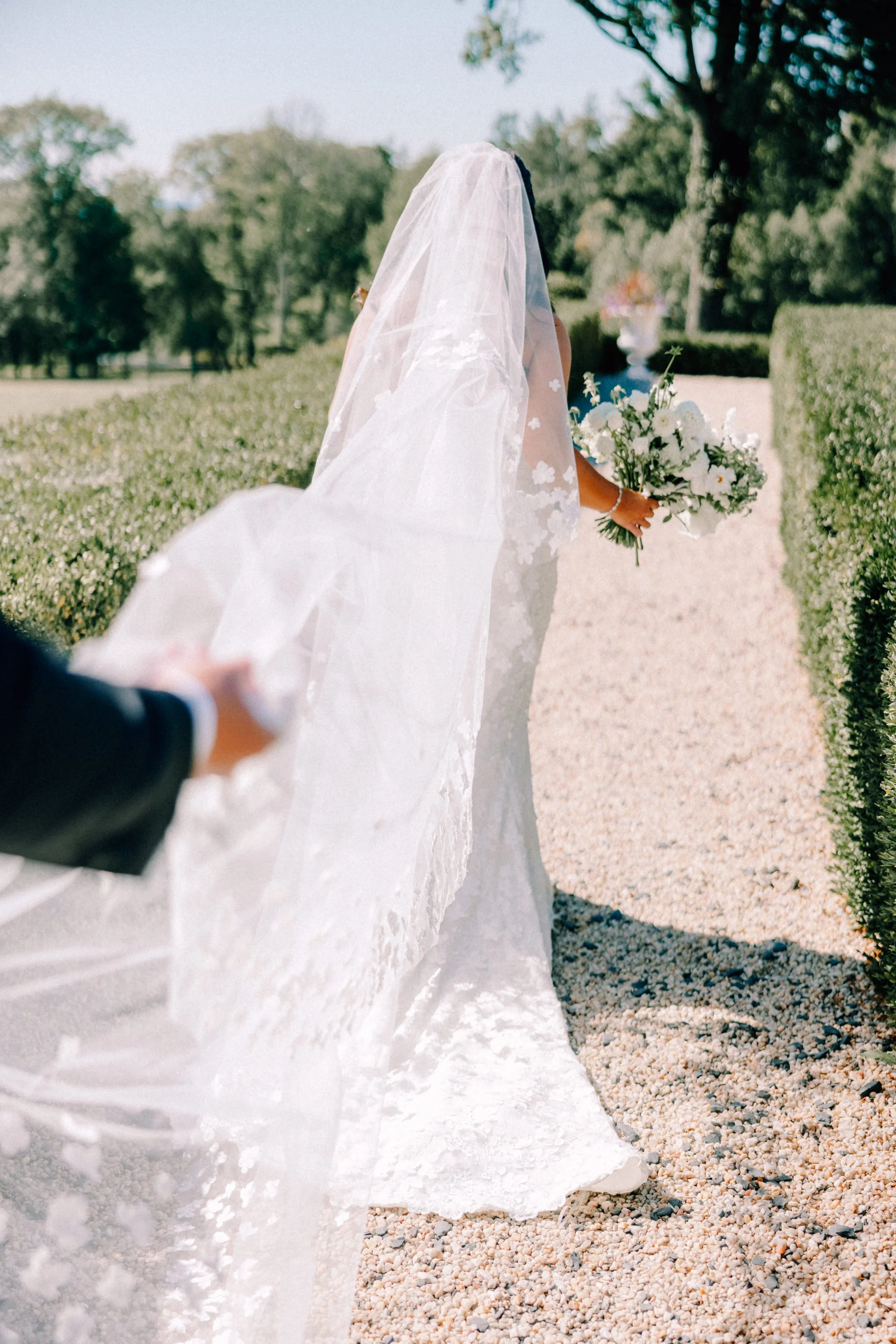 photograph of bride walking away while the hand of the groom is in frame holding up her cathedral length veil at Glenmere Mansion on their wedding day