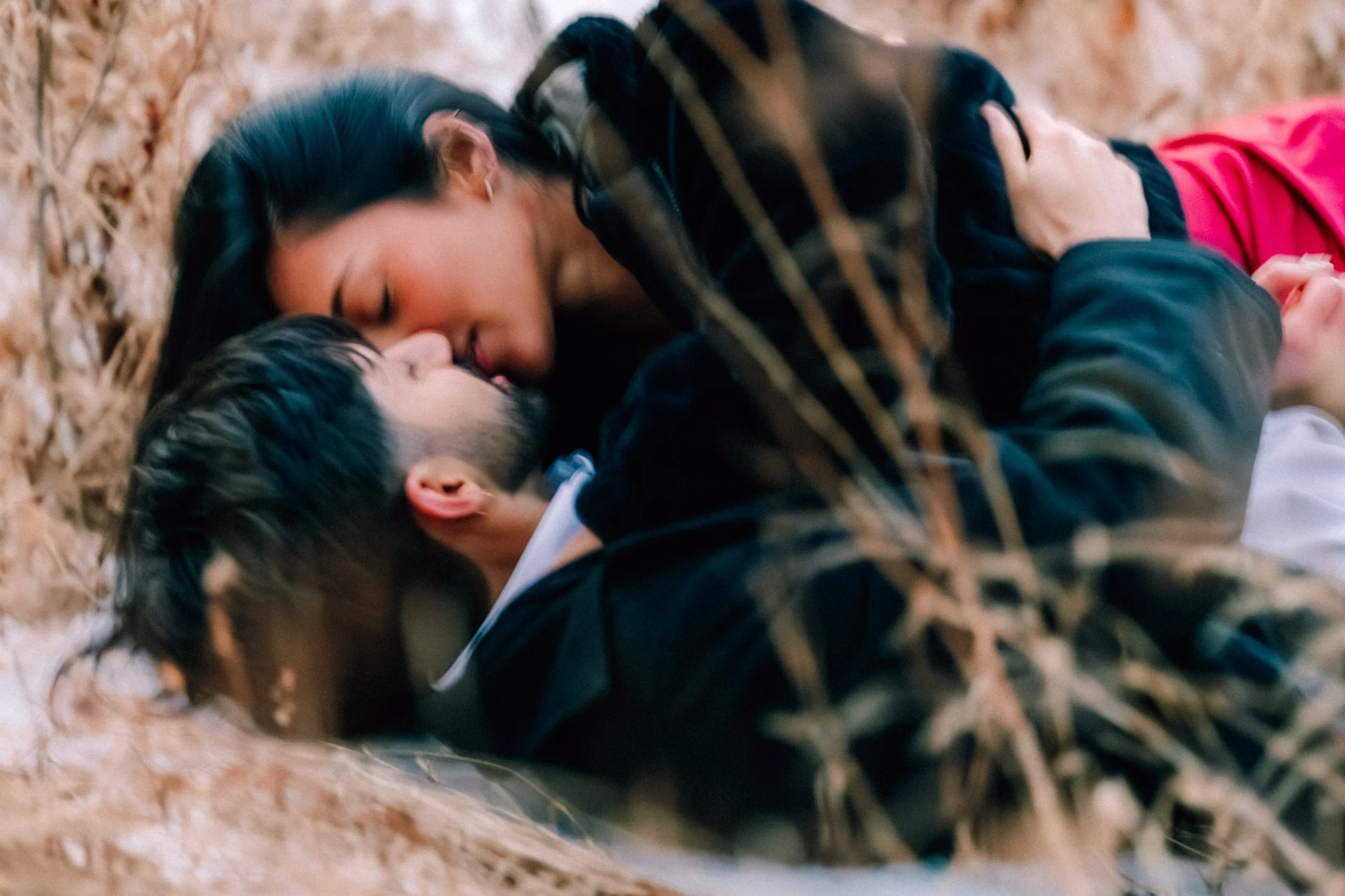 A couple lying on the ground in the snow, close to each other, about to kiss in a natural outdoor setting with dried grass during their surprise proposal and engagement photo shoot at Mohonk Mountain House.