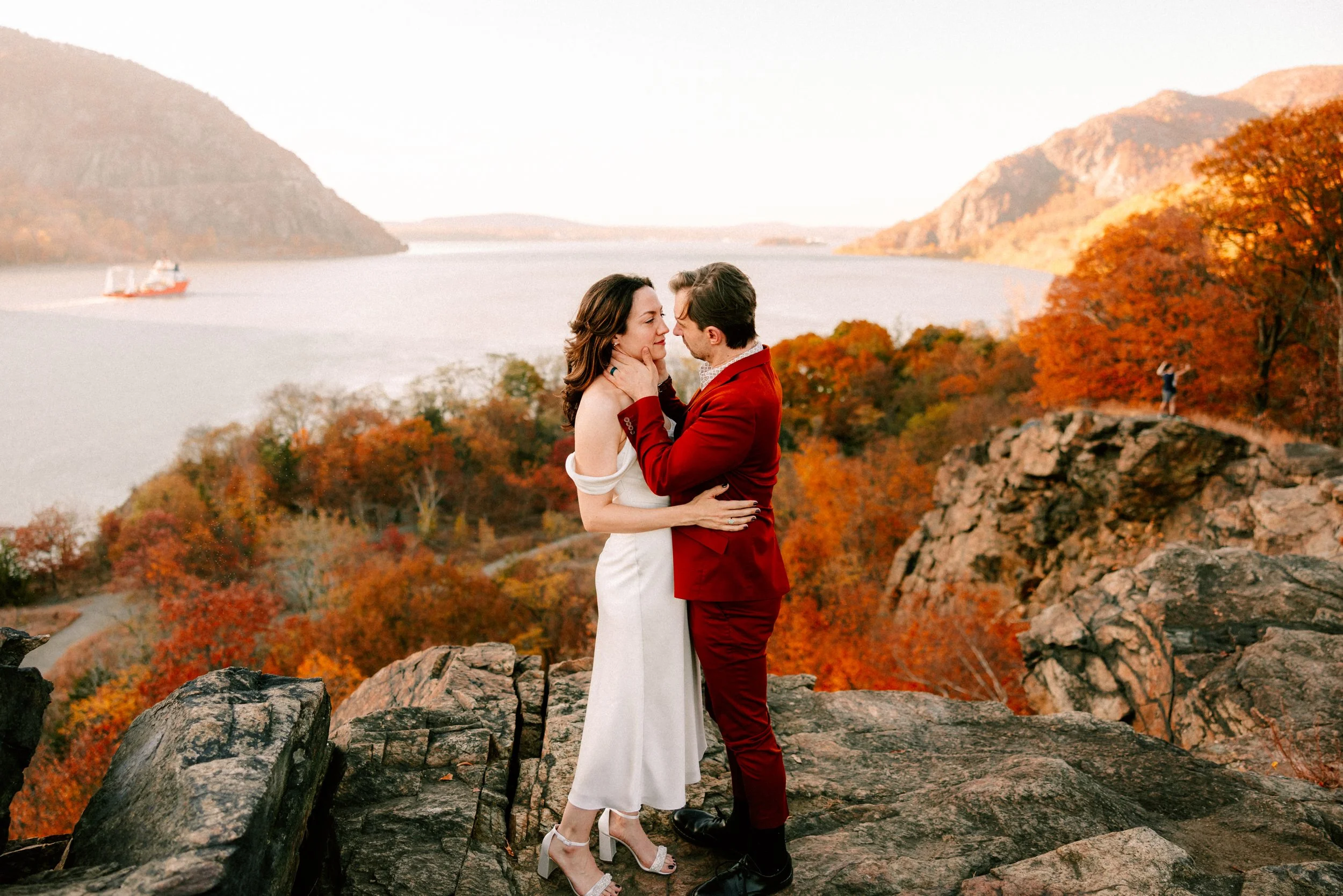 couple embrace at little stony point with the fall foliage behind them during their engagement shoot