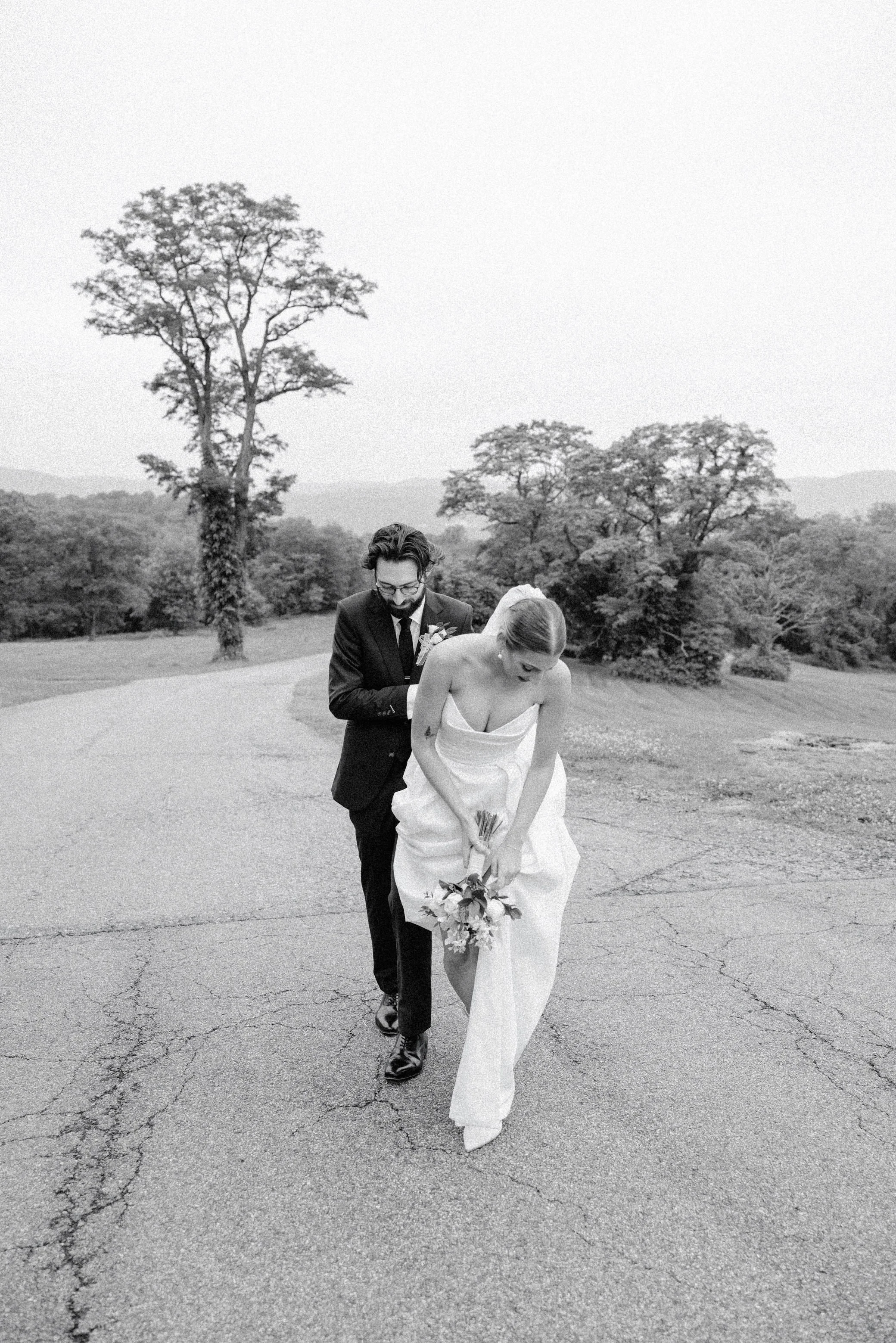 couple walking up hill while gathering her dress on their wedding day at the garrison