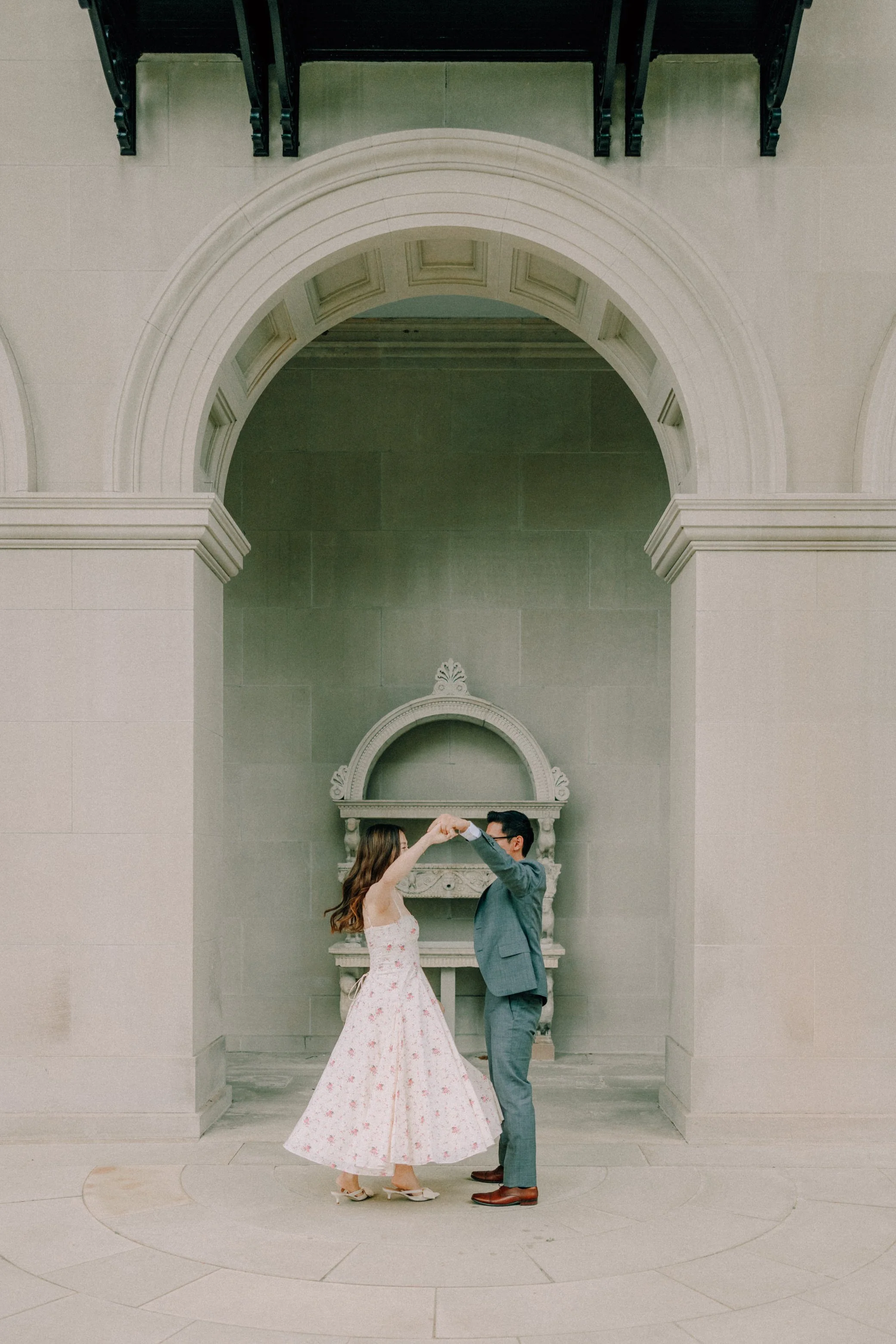 engaged couple standing under an arch face each other and hold their hands together to spin during their engagement photography shoot at vanderbilt mansion