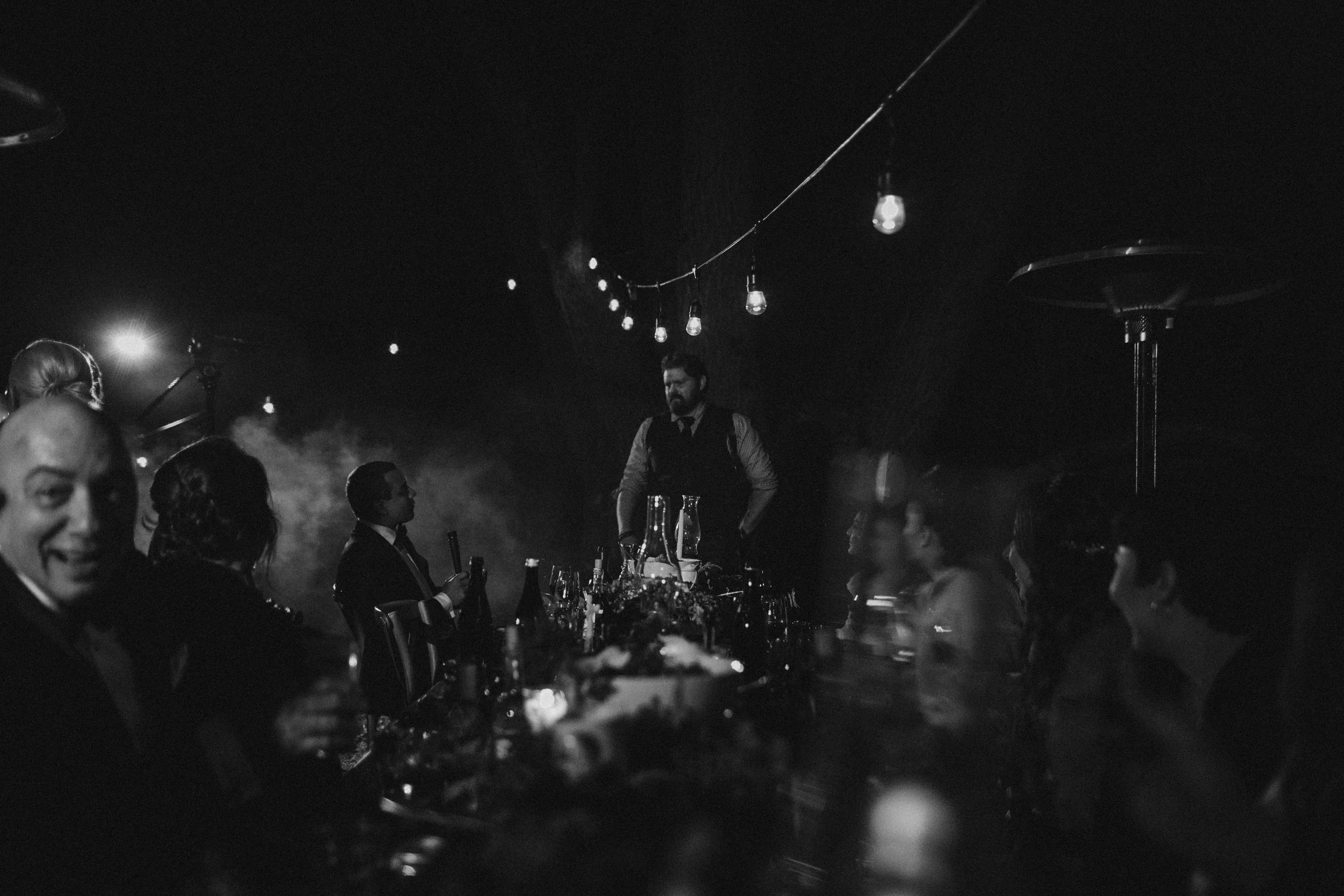 chef james gop of heirloom fire explains his menu to micro wedding guests dining outside under the lights