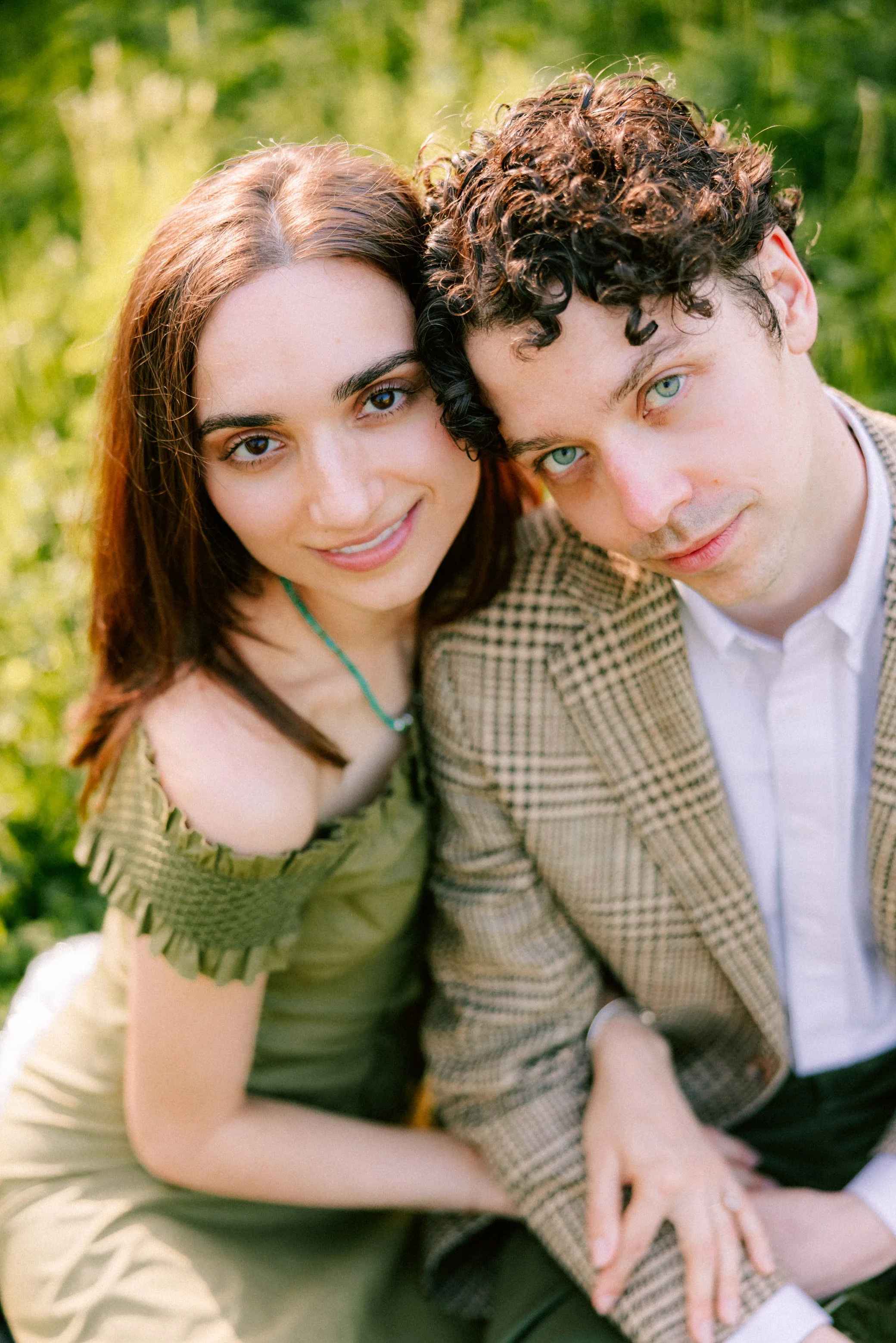 couple sitting in grass looking up into the camera during their engagement photography session at camptown new york