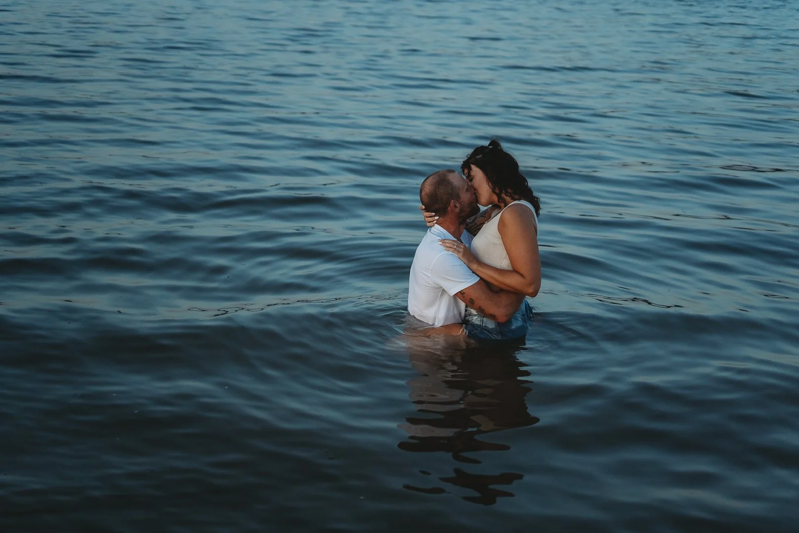 A couple embracing and kissing in waist-deep water.