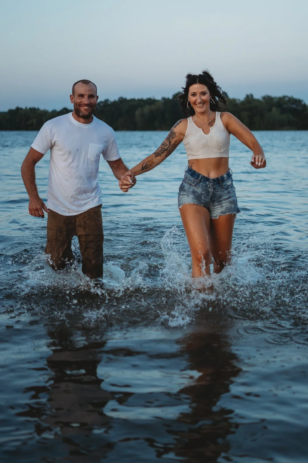 Man and woman holding hands while splashing in the water at the beach.