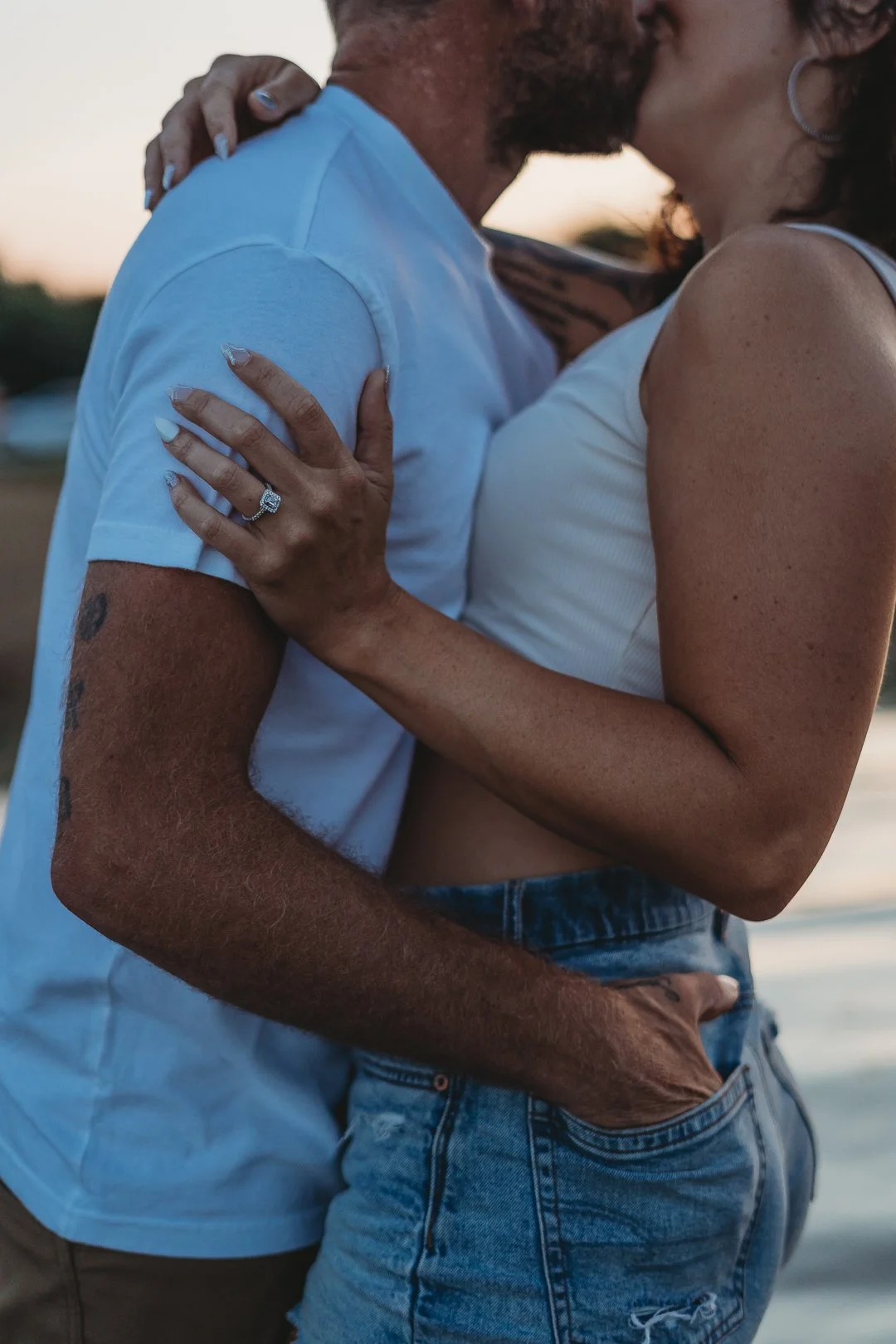 Close-up of a couple embracing; a woman with an engagement ring touching a man's arm.