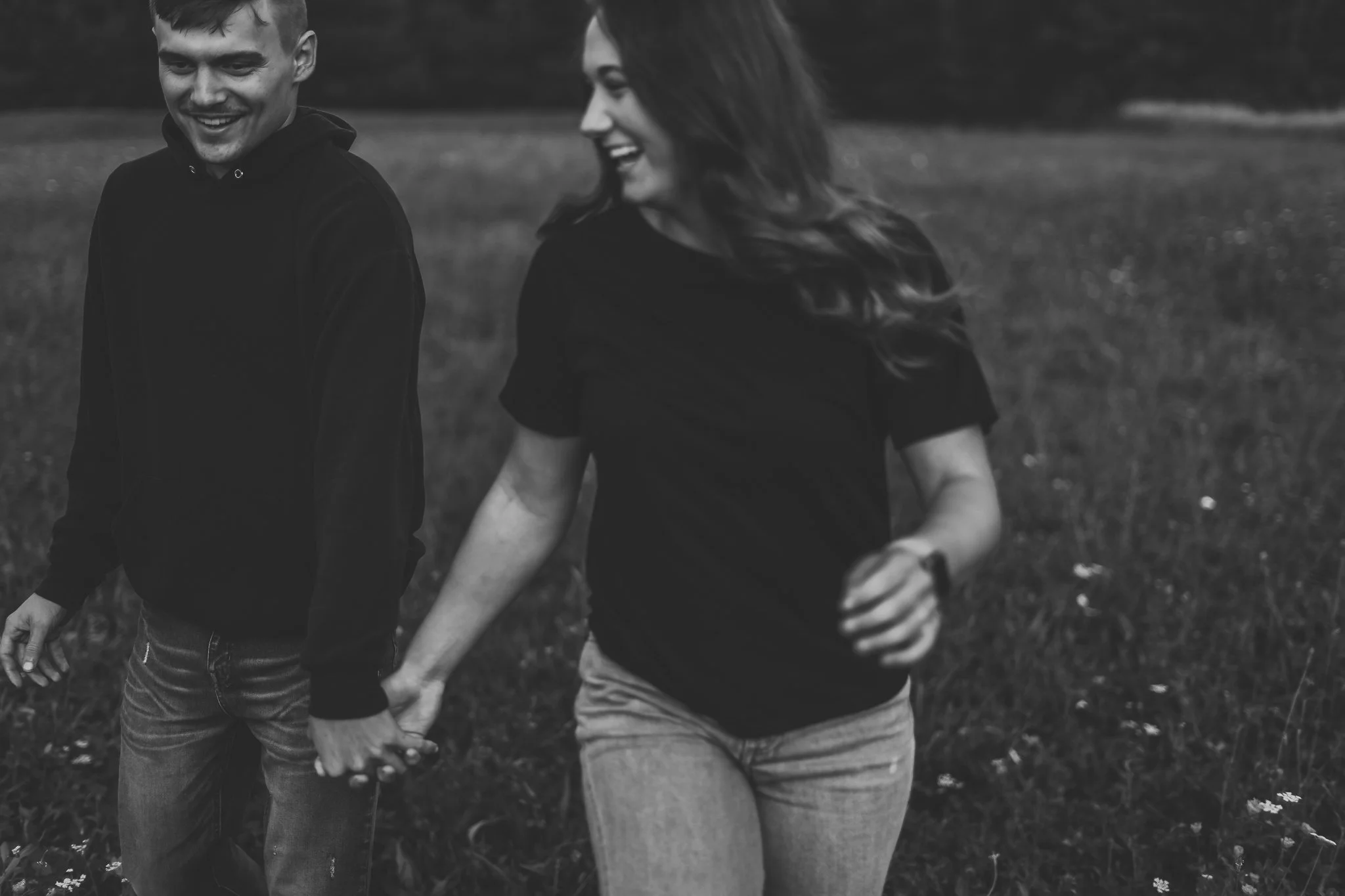 Black and white photo of a smiling couple holding hands while walking in a field.