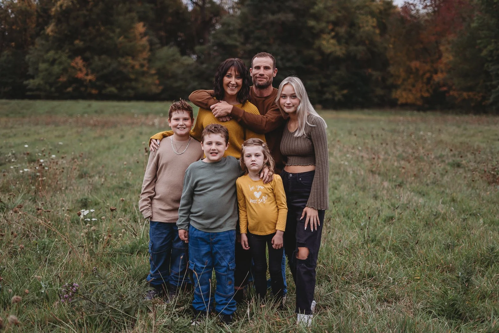 Family of six posing in a grassy field with trees in the background.