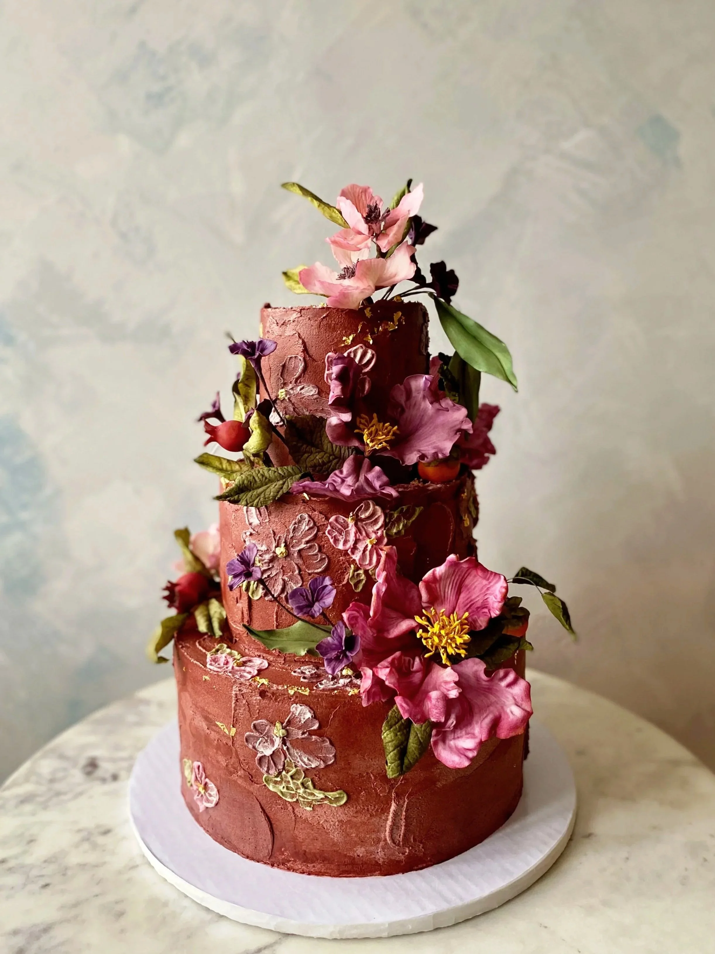Dark chocolate vegan wedding cake with romantic painted icing flowers and sugar flower peonies, pomegranates, and persimmons. 