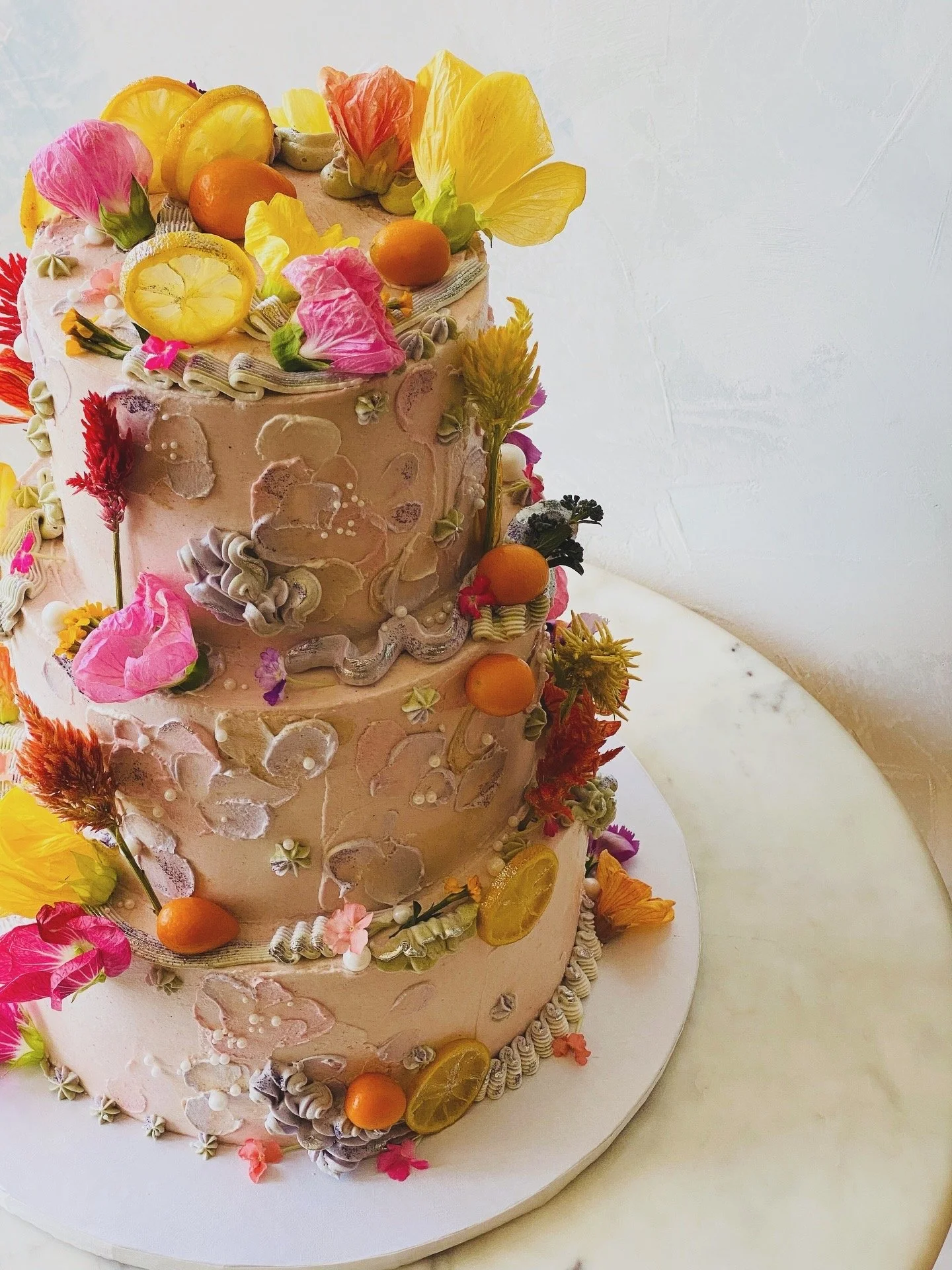 Creative abstract piping with colorful edible flowers, citrus, and pearls on a gluten-free wedding cake. 
