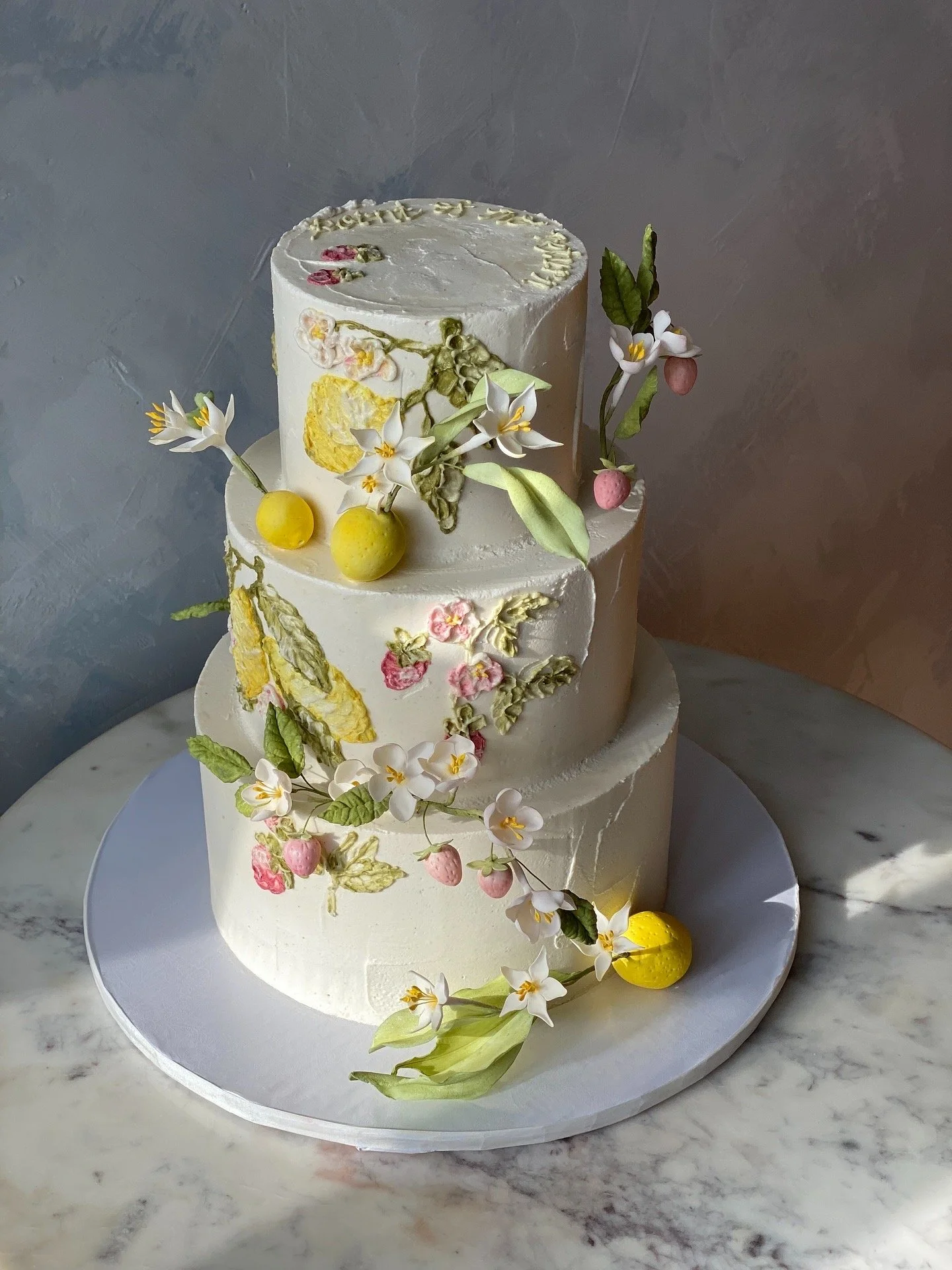 Three tiers of buttercream, lemon, strawberry icing design with sculpted fruit and flowers and a custom piped message. 