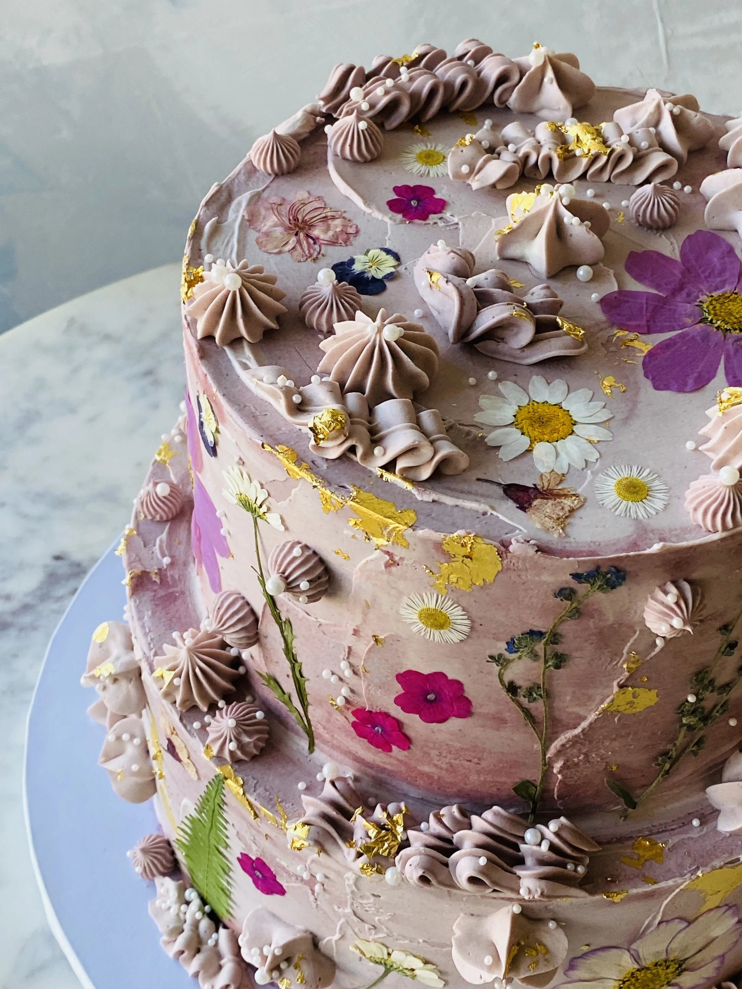 Purple plum cake with contemporary piping and pressed edible flowers.