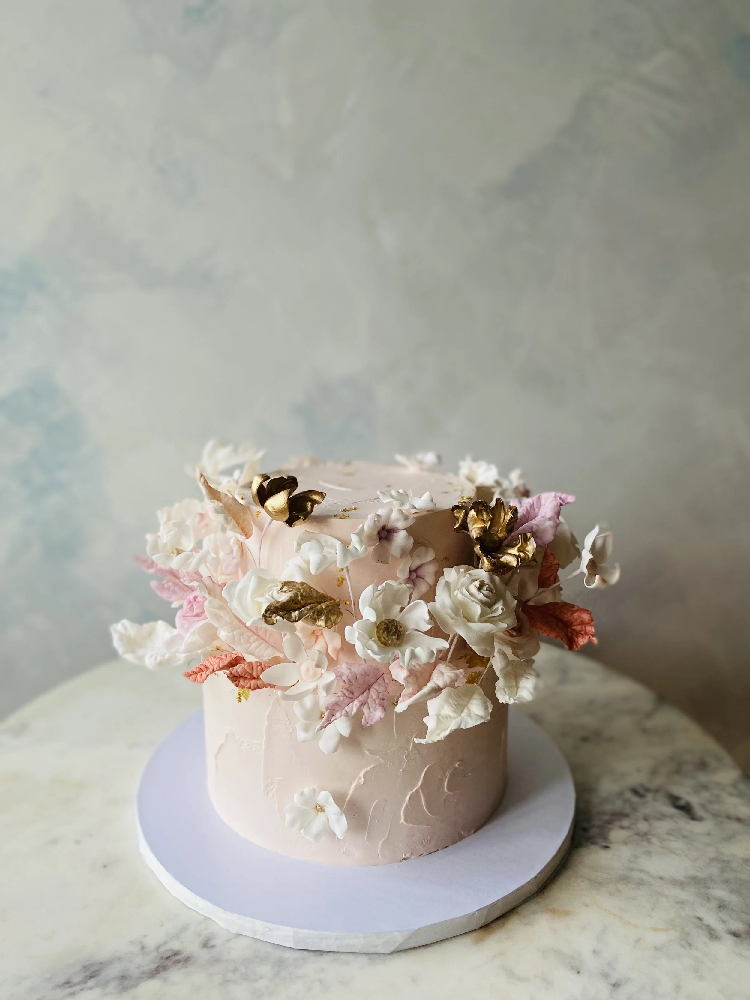 Romantic pink buttercream gluten-free babyshower cake with sugar flowers, gold, and unique colors. 
