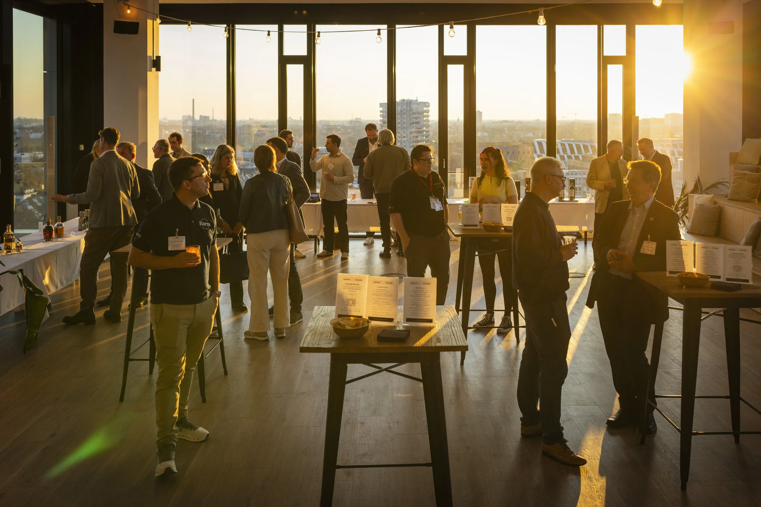 People networking and socializing at a sunset reception in a high-rise venue with large windows and city views.