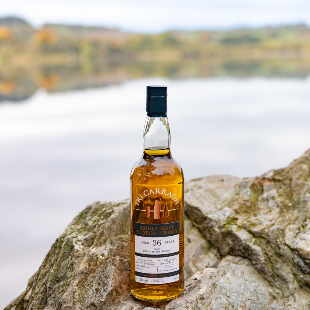 A bottle of single malt Scotch whisky placed on a large rock with a lake and trees in the background.