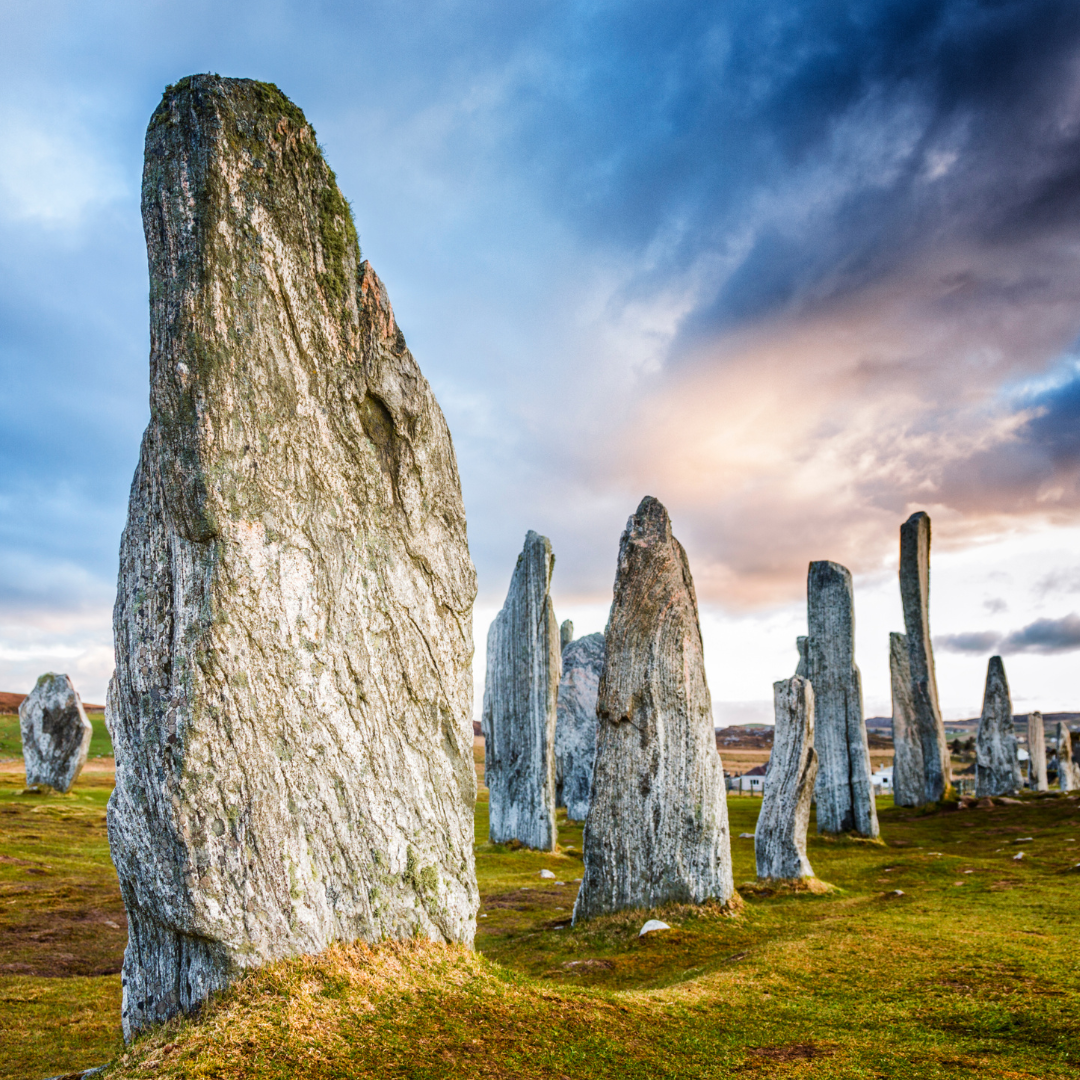 Stone circle standing stones on grassy landscape during sunset with cloudy sky.