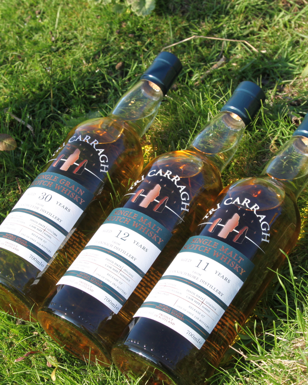 Three bottles of Tricarragh single malt Scotch whisky lying on grass, aged 30, 12, and 11 years.