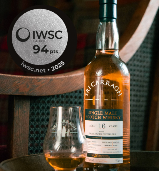 A bottle of Tri Carragh single malt Scotch whisky aged 16 years on a table next to a glass filled with whisky, with a circular IWSC award sticker in the background.