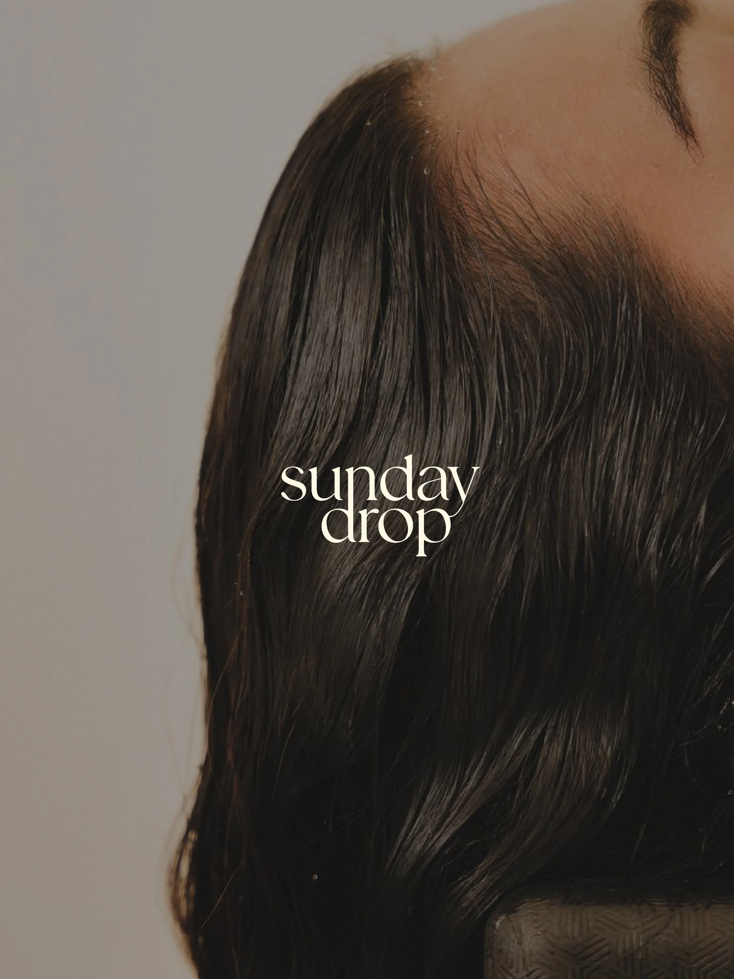 Close-up of dark, shiny, wavy hair with the text 'sunday drop' overlayed