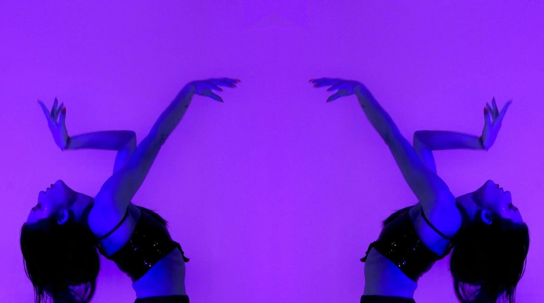 A mirrored image of a woman with long dark hair, wearing a black crop top, striking a dance pose against a purple and blue gradient background.