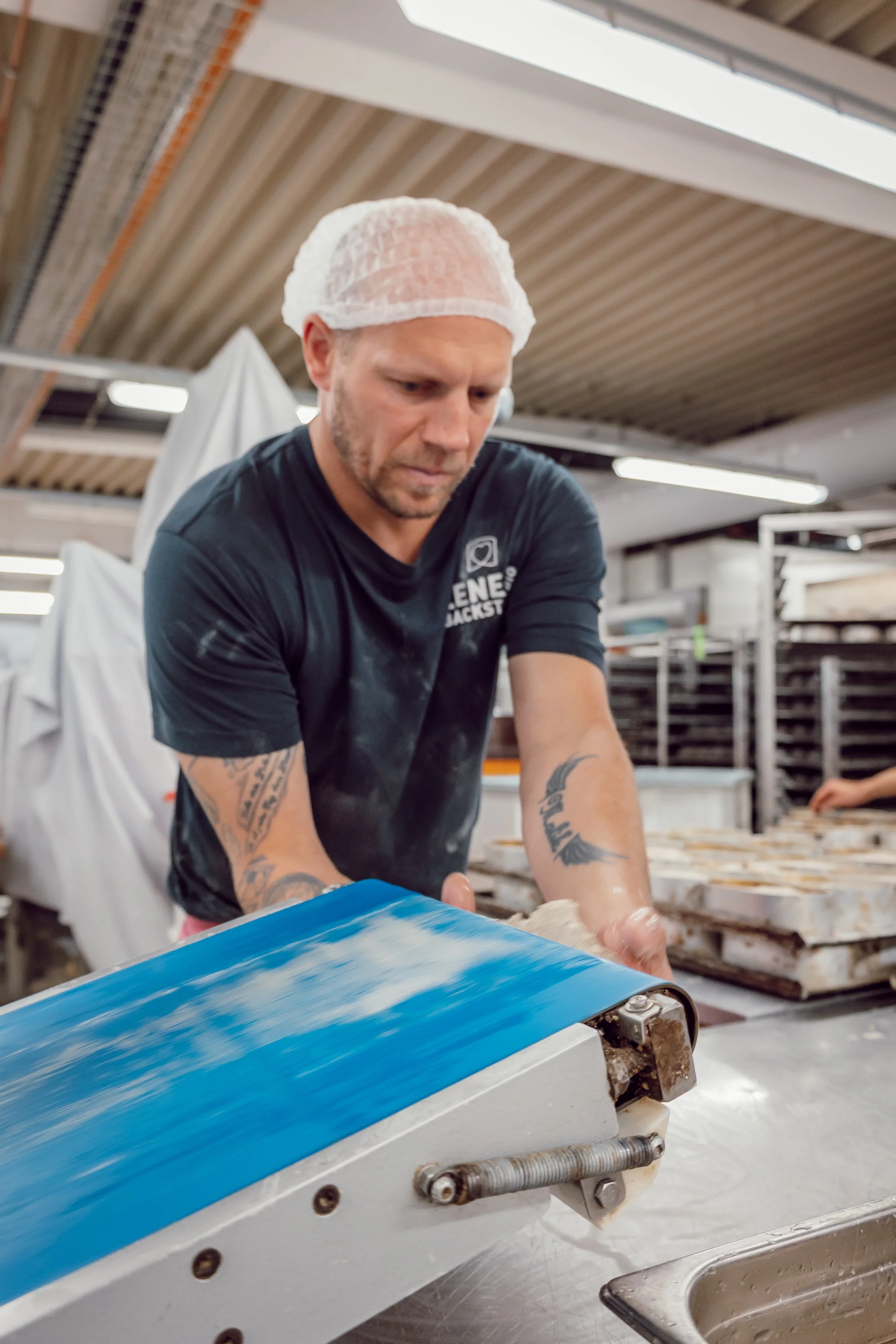 Über ein Rollband bekommt ein Bäcker portionierte Teigmasse auf die Arbeitsfläche geliefert.