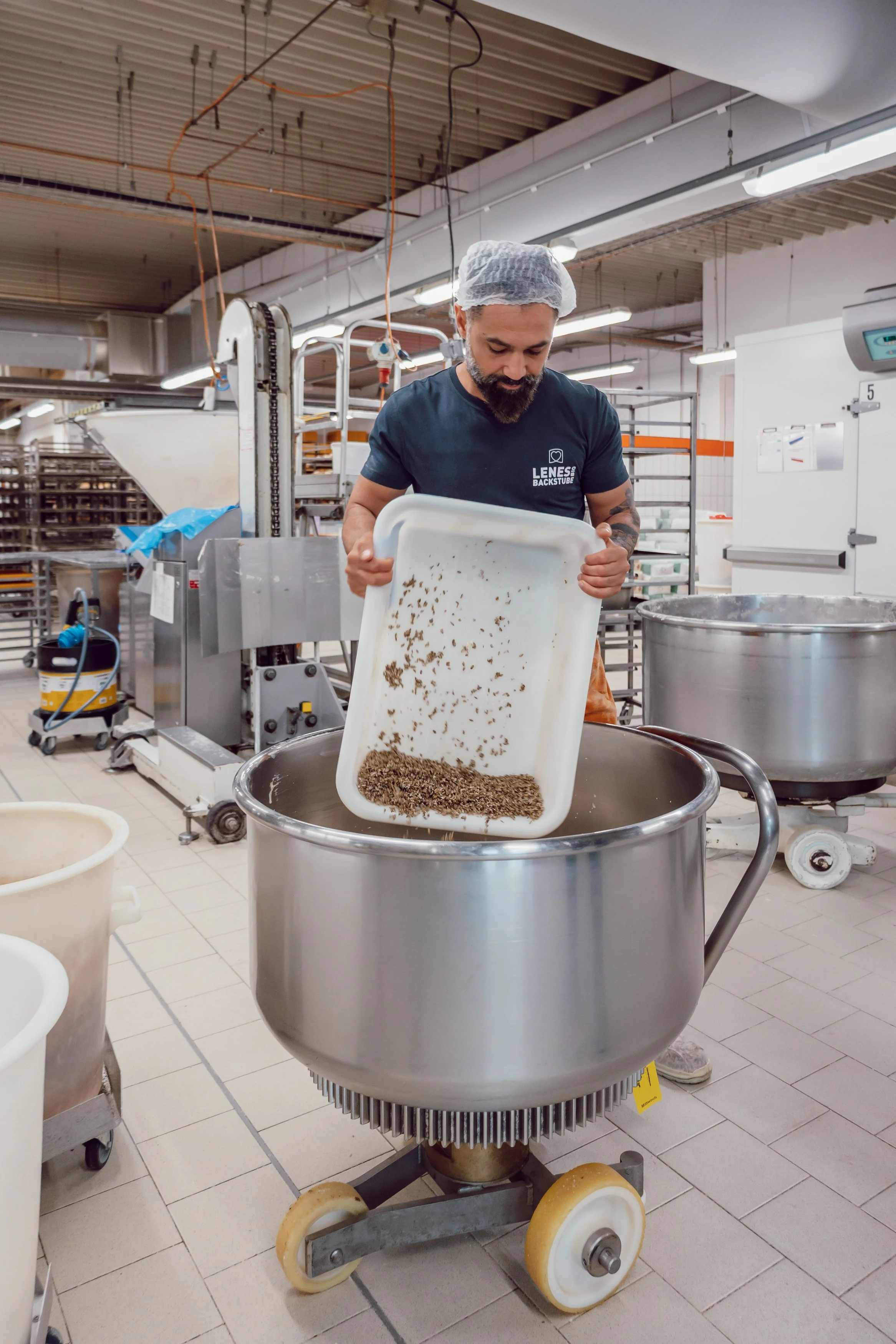 Ein Bäcker von Lenes Bio Backstube gibt Saaten in eine Aluschale. Die Saaten sind Zutaten für das Bio Brot.