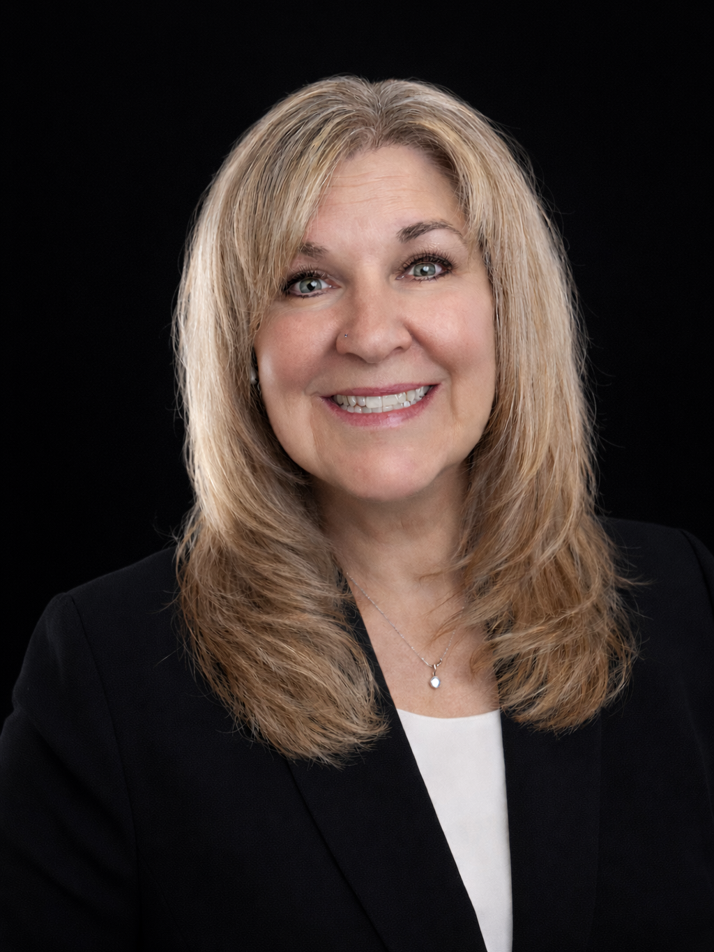 A woman with blonde hair, wearing a black blazer and a white shirt, smiling against a black background.