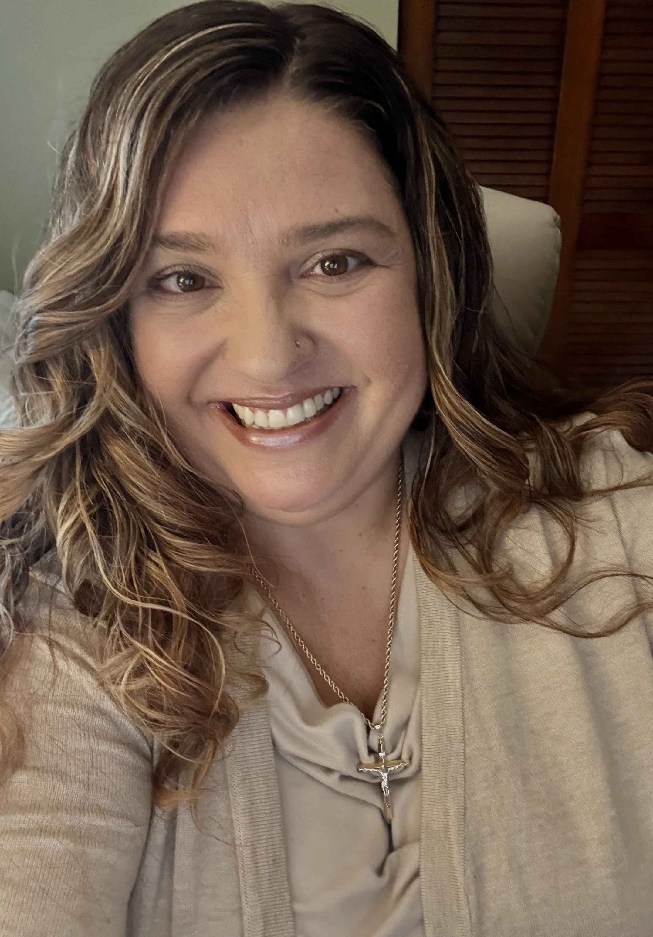 Woman with curly hair smiling, wearing a floral dress, standing amidst lush green plants.