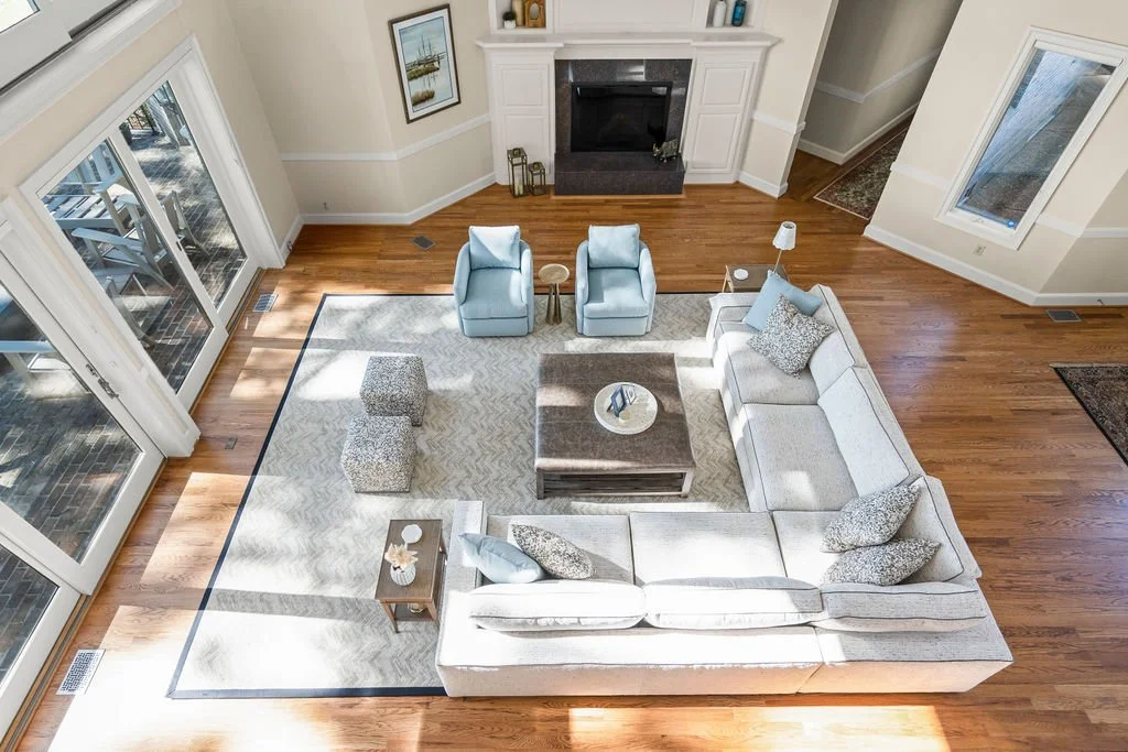 Spacious waterfront living room designed by AWH Interiors in Williamsburg, featuring soft blue accents, layered neutrals, and natural wood tones that echo the coastal surroundings.