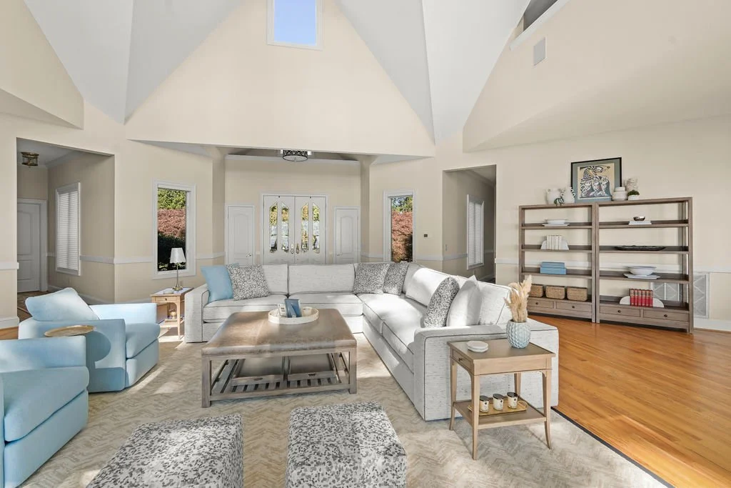 Spacious waterfront living room designed by AWH Interiors in Williamsburg, featuring soft blue accents, layered neutrals, and natural wood tones that echo the coastal surroundings.