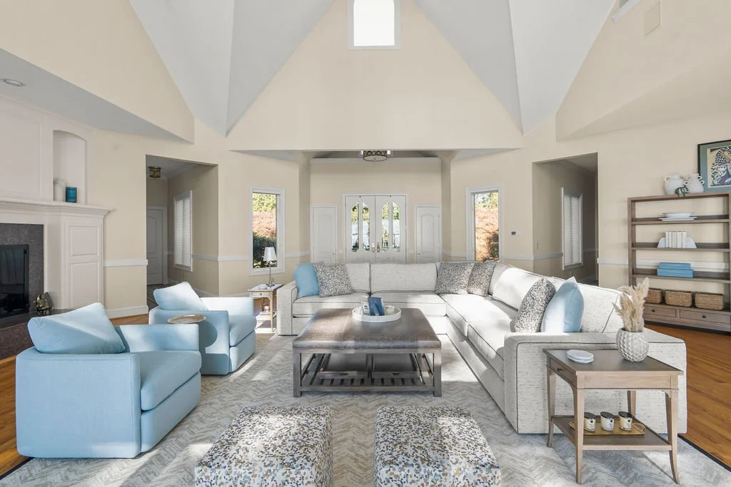 Spacious waterfront living room designed by AWH Interiors in Williamsburg, featuring soft blue accents, layered neutrals, and natural wood tones that echo the coastal surroundings.