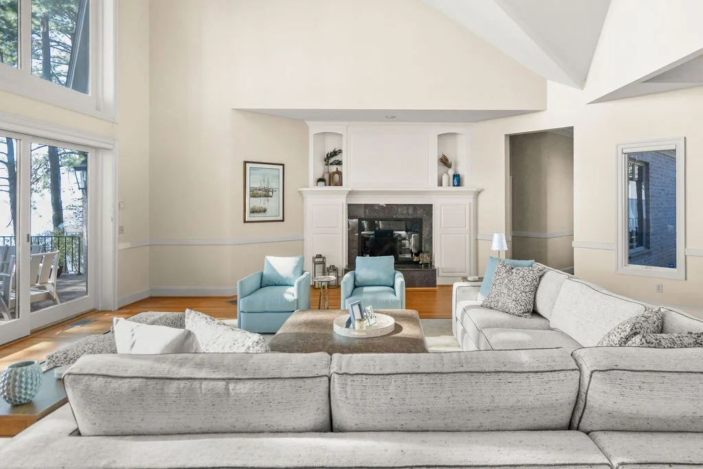 Spacious waterfront living room designed by AWH Interiors in Williamsburg, featuring soft blue accents, layered neutrals, and natural wood tones that echo the coastal surroundings.