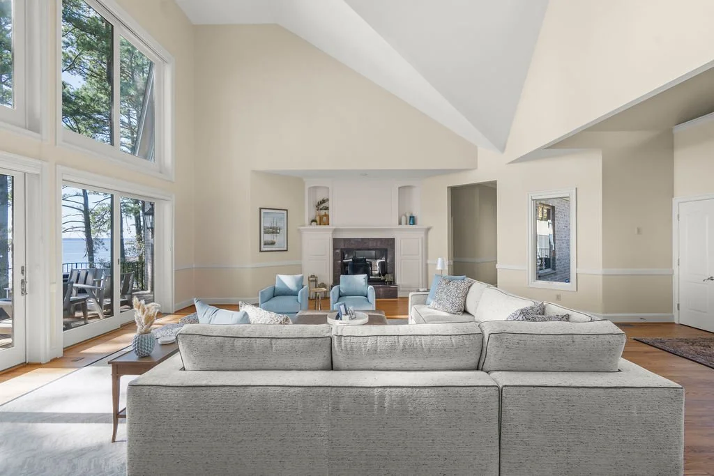 Spacious waterfront living room designed by AWH Interiors in Williamsburg, featuring soft blue accents, layered neutrals, and natural wood tones that echo the coastal surroundings.