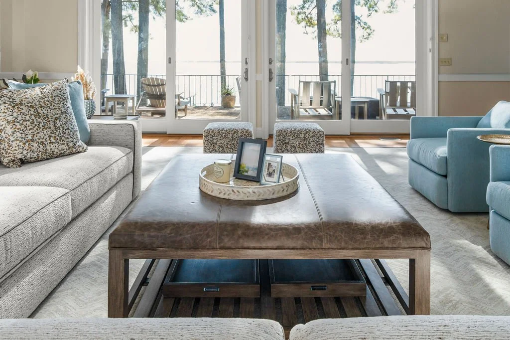 Spacious waterfront living room designed by AWH Interiors in Williamsburg, featuring soft blue accents, layered neutrals, and natural wood tones that echo the coastal surroundings.